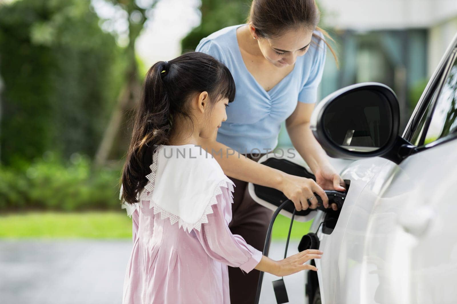 Progressive lifestyle of mother and daughter who have just returned from school in an electric vehicle that is being charged at home. Electric vehicle powered by sustainable clean energy.