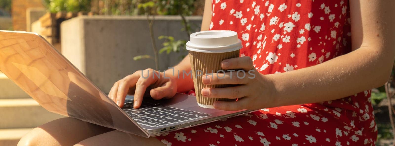 Unrecognizable Young woman in red dress drinking Take away coffee in craft recycling paper cup with laptop. Freelancer's place of work. Study and work online. Remote business education. View webinar. E-learning Workstation on wooden bench. Mockup Coffee break. Making plans for next week year. Being mindful reducing stress and slowing-down