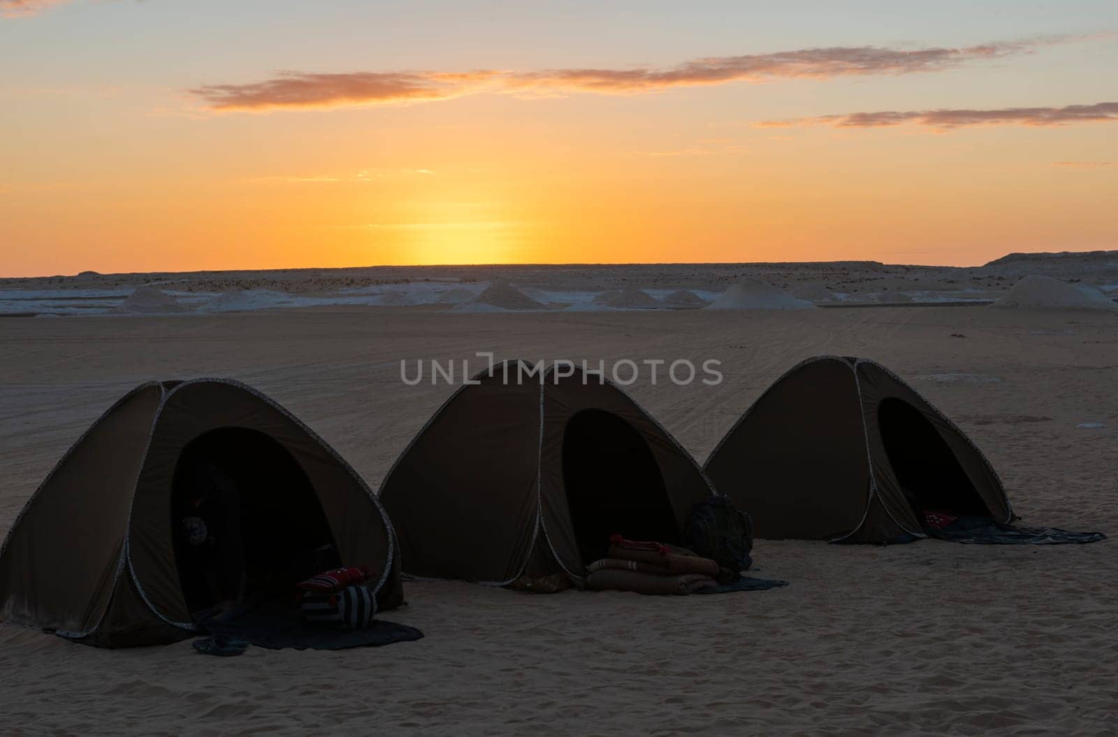 Landscape scenic view of desolate barren western desert campsite in Egypt with tents camping against sunrise background