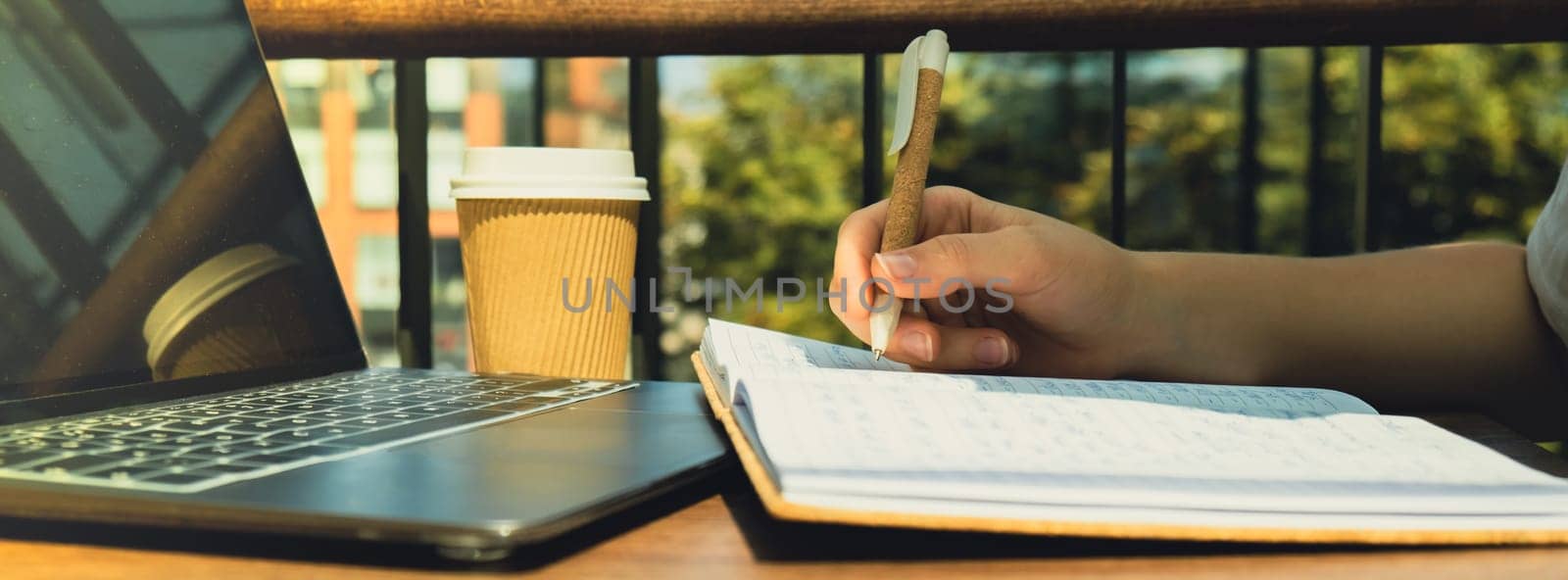Unrecognizable Young woman study at wooden table in shopping mall food court. Drinking coffee from paper cup. Student making homework Female hands writing on notebook gratitude journal self reflection self discovery in Co-Working Space. Goals, to-do list in the modern office building