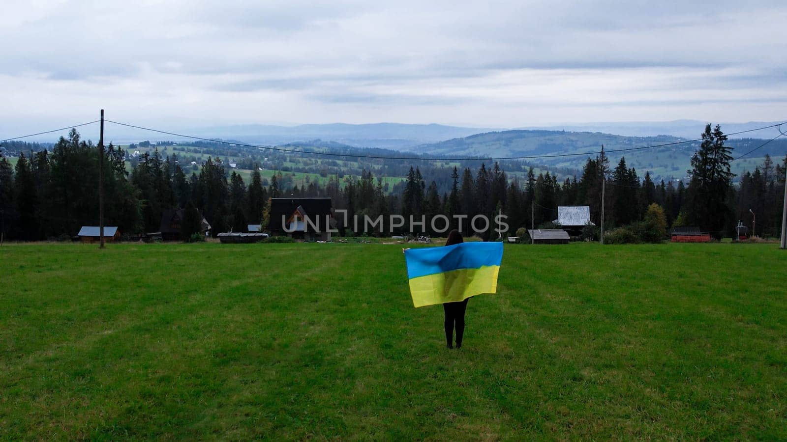 Woman with Ukrainian national flag waving Patriotism Aerial view of Zakopane town underneath Tatra Mountains taken from the Gubalowka mountain range. Drone High mountains and green hills in summer or spring. Scenic mountain view in Poland. Travel tourist destinations