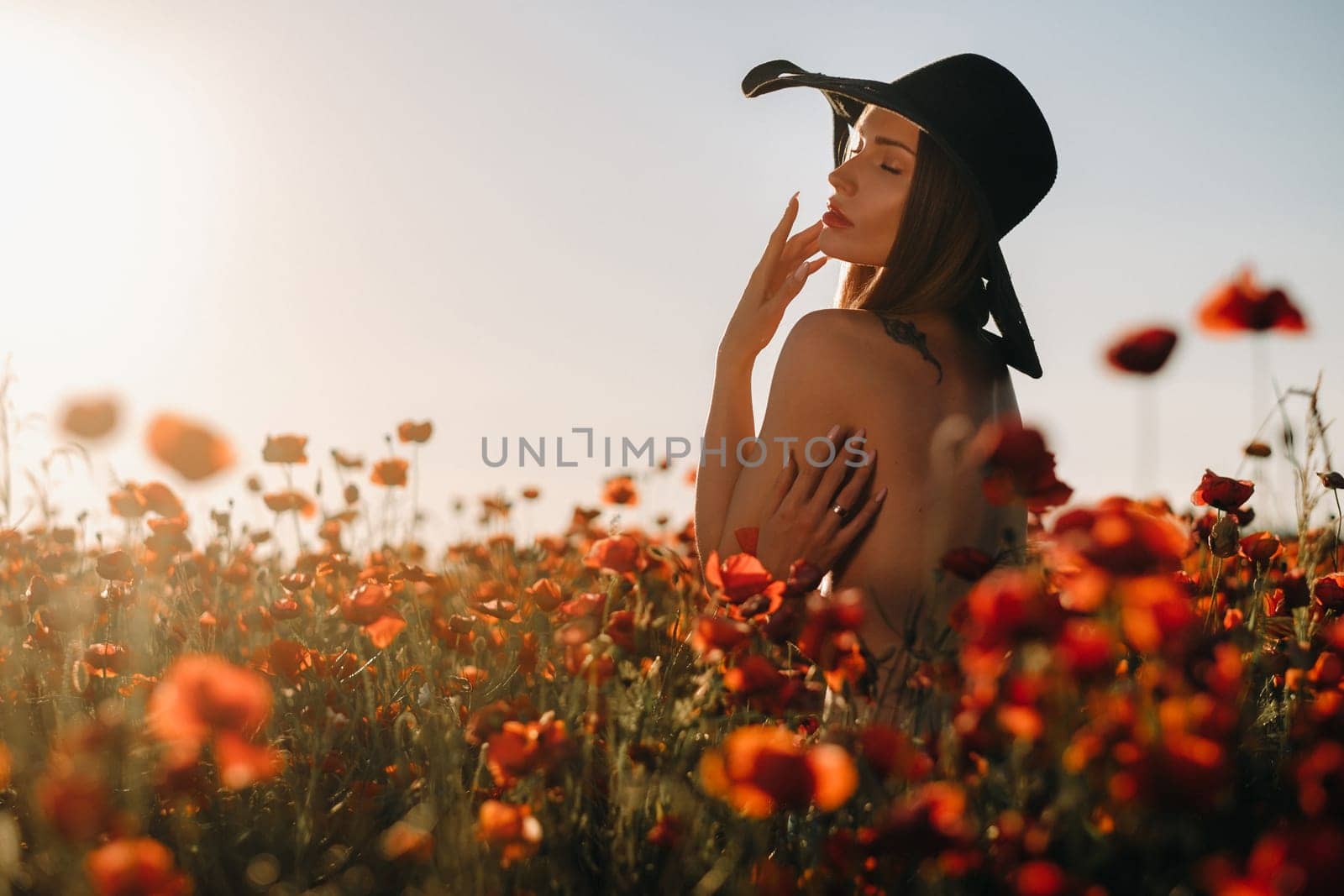 naked girl from behind in a black hat in a poppy field at sunset.