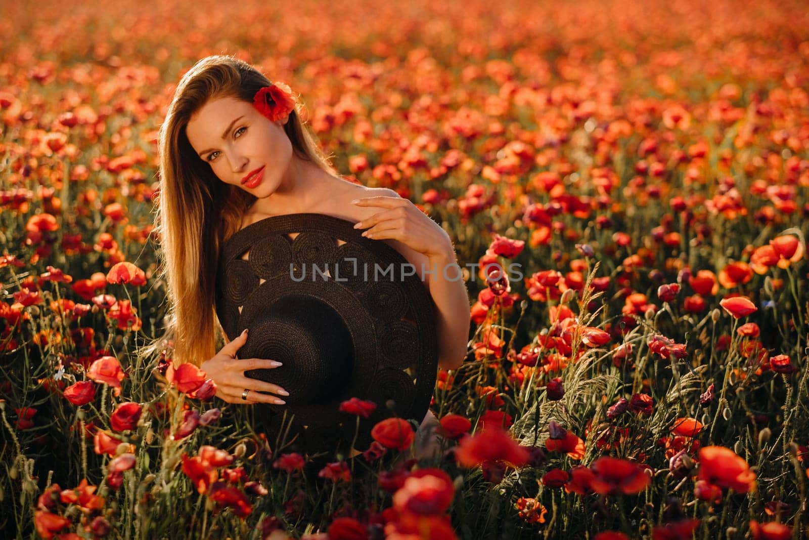 naked girl with a black hat in her hands in a poppy field at sunset by Lobachad