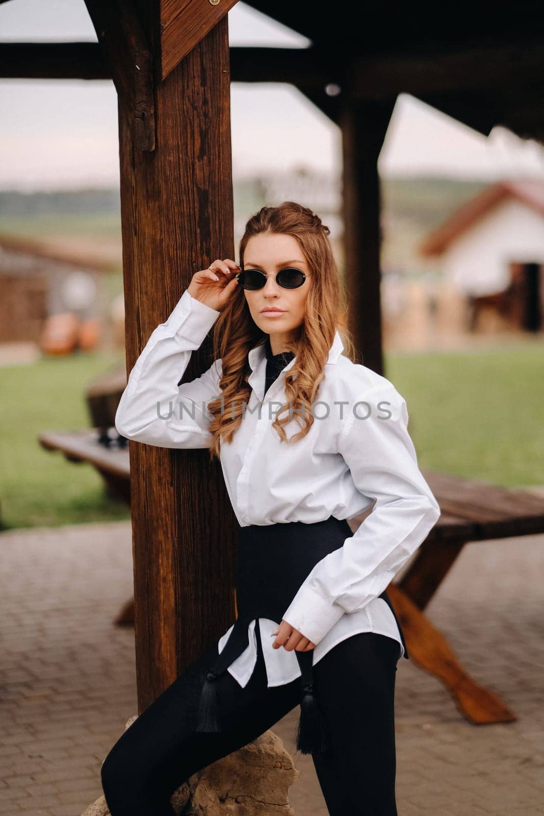 A stylish girl in a white shirt and sunglasses standing on the street during the day by Lobachad