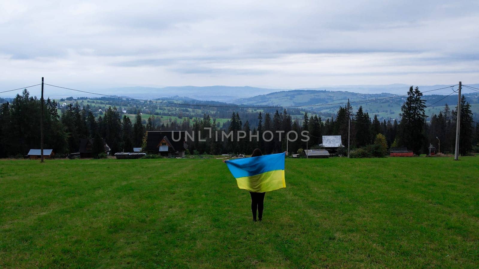 Woman with Ukrainian national flag waving Patriotism Aerial view of Zakopane town underneath Tatra Mountains taken from the Gubalowka mountain range. Drone High mountains and green hills in summer or spring. Scenic mountain view in Poland. Travel tourist destinations