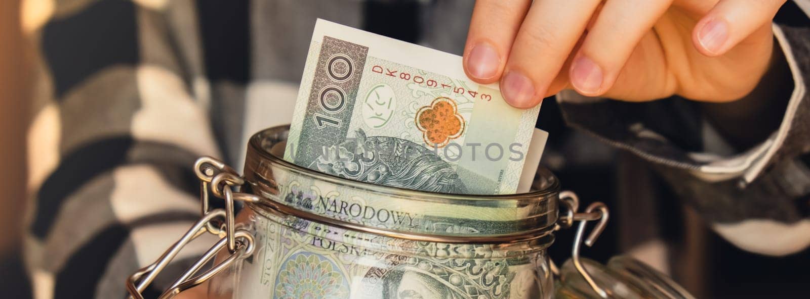 Polish zloty banknote saving money in glass jar. Unrecognizable woman moderate consumption and economy Collecting money. Tips. Business, finance, saving, banking and people concept. Extra money, passive income. Saving for travel, crisis, house, car, education, retirement Banner