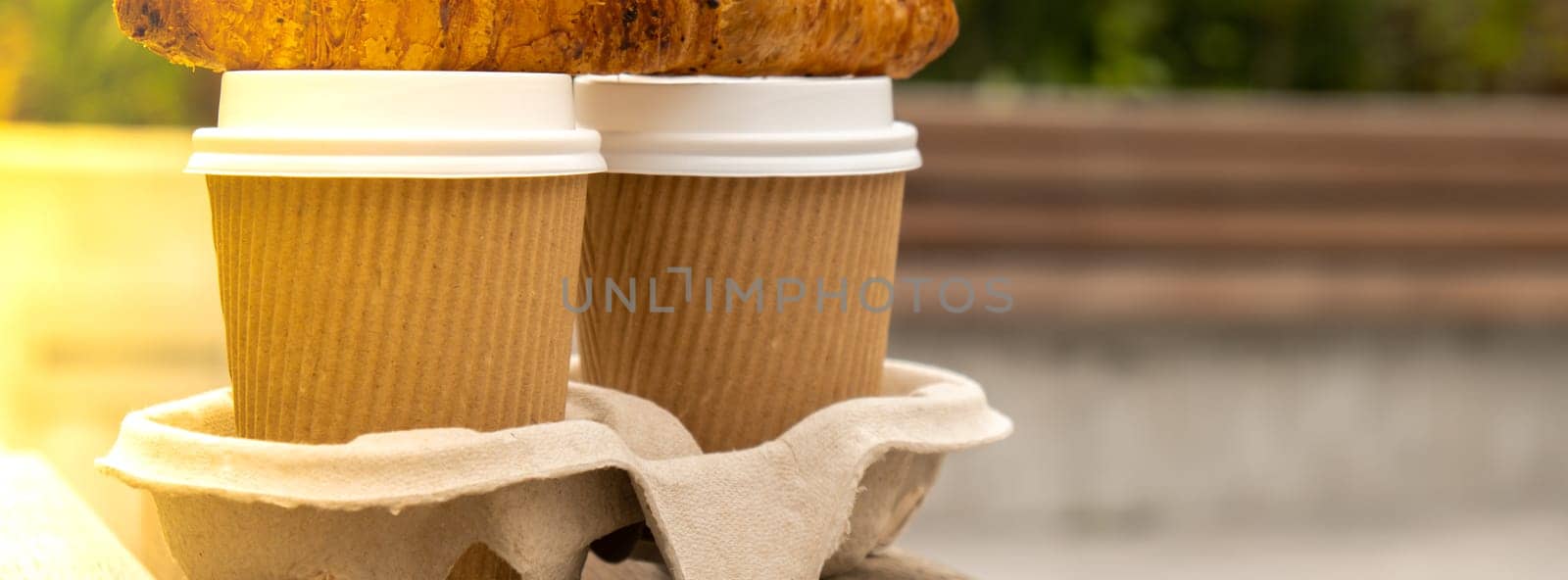Fresh baked chocolate croissant on Two paper cups with lid for tea to go. Breakfast Coffee take away on the table. Take-out coffees with brown paper cup holder. Brown safety cardboard collars. Take away box for cups. Cardboard tray