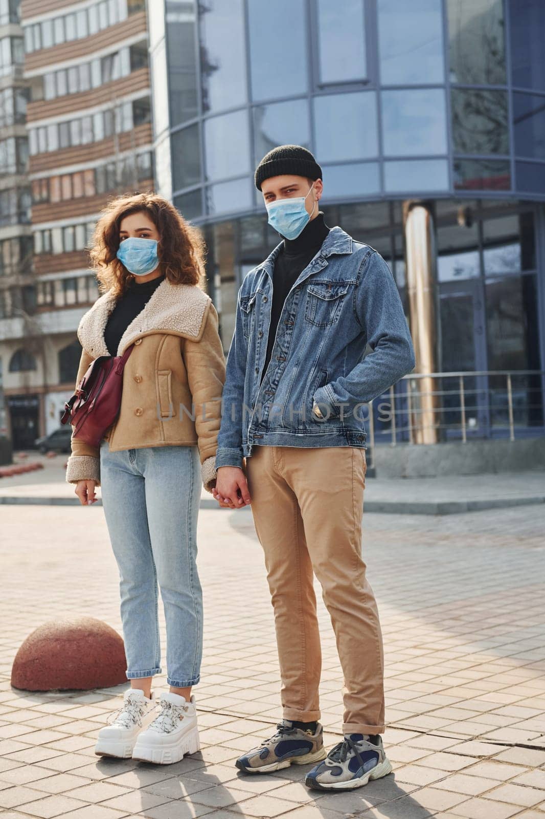 Couple in protective masks have a walk outdoors in the city near business building at quarantine time. Conception of coronavirus.