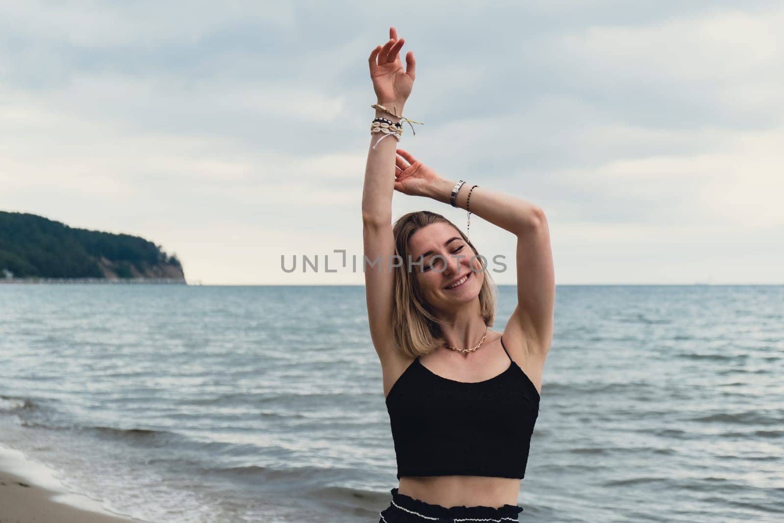 Young woman standing on blurred beachside background. Attractive female enjoying walking the sea shore. travel and active lifestyle concept. Springtime. Relaxation, youth, love, lifestyle solitude with nature. Wellness wellbeing mental health inner peace Slow life digital detox