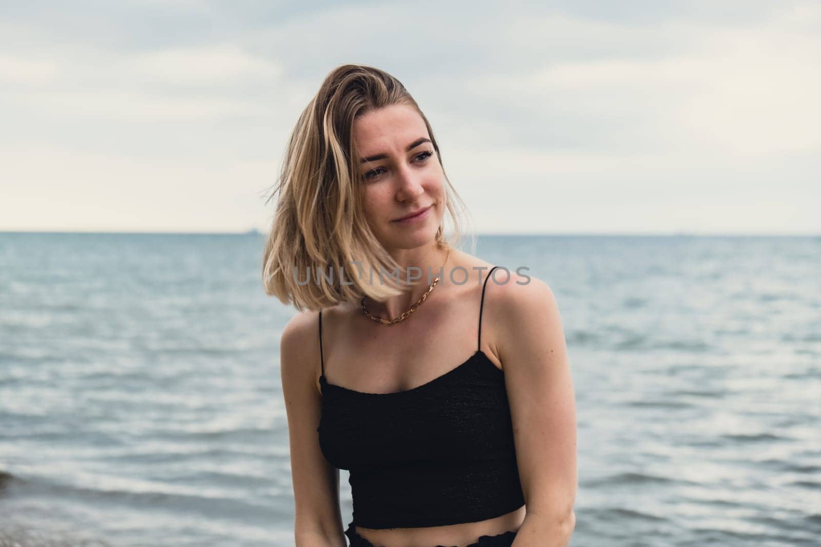 Young woman standing on blurred beachside background. Attractive female enjoying walking the sea shore. travel and active lifestyle concept. Springtime. Relaxation, youth, love, lifestyle solitude with nature. Wellness wellbeing mental health inner peace Slow life digital detox