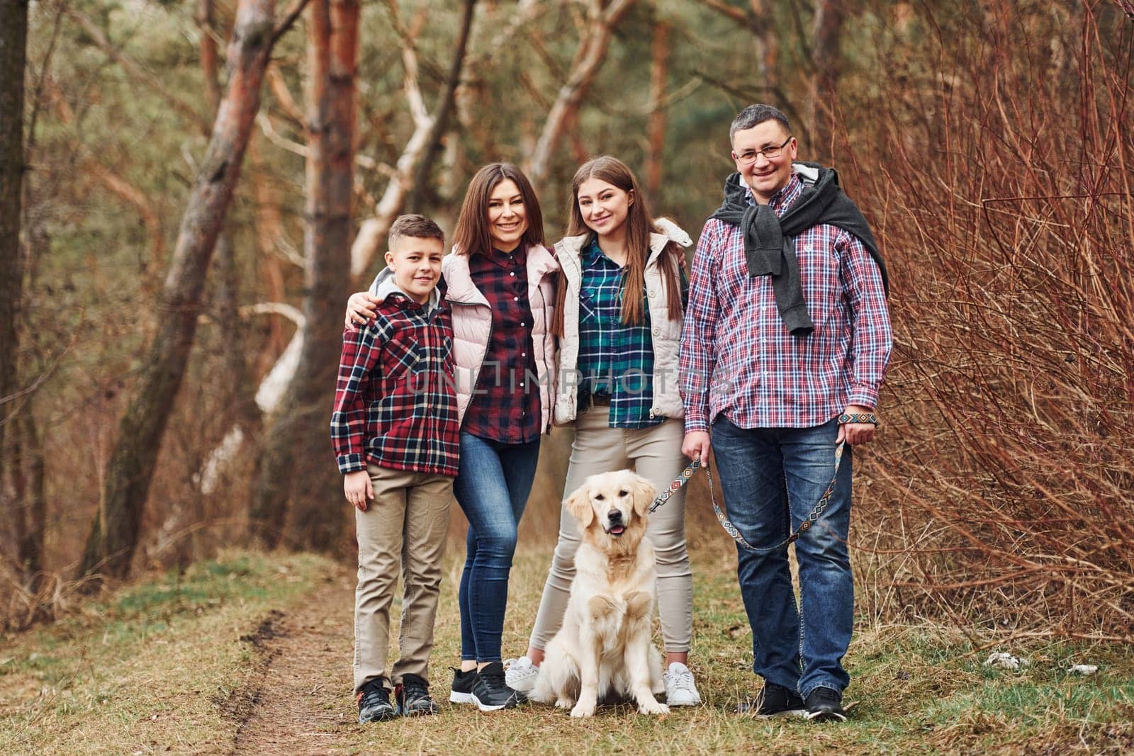 Happy family standing together with their dog outdoors in forest by Standret