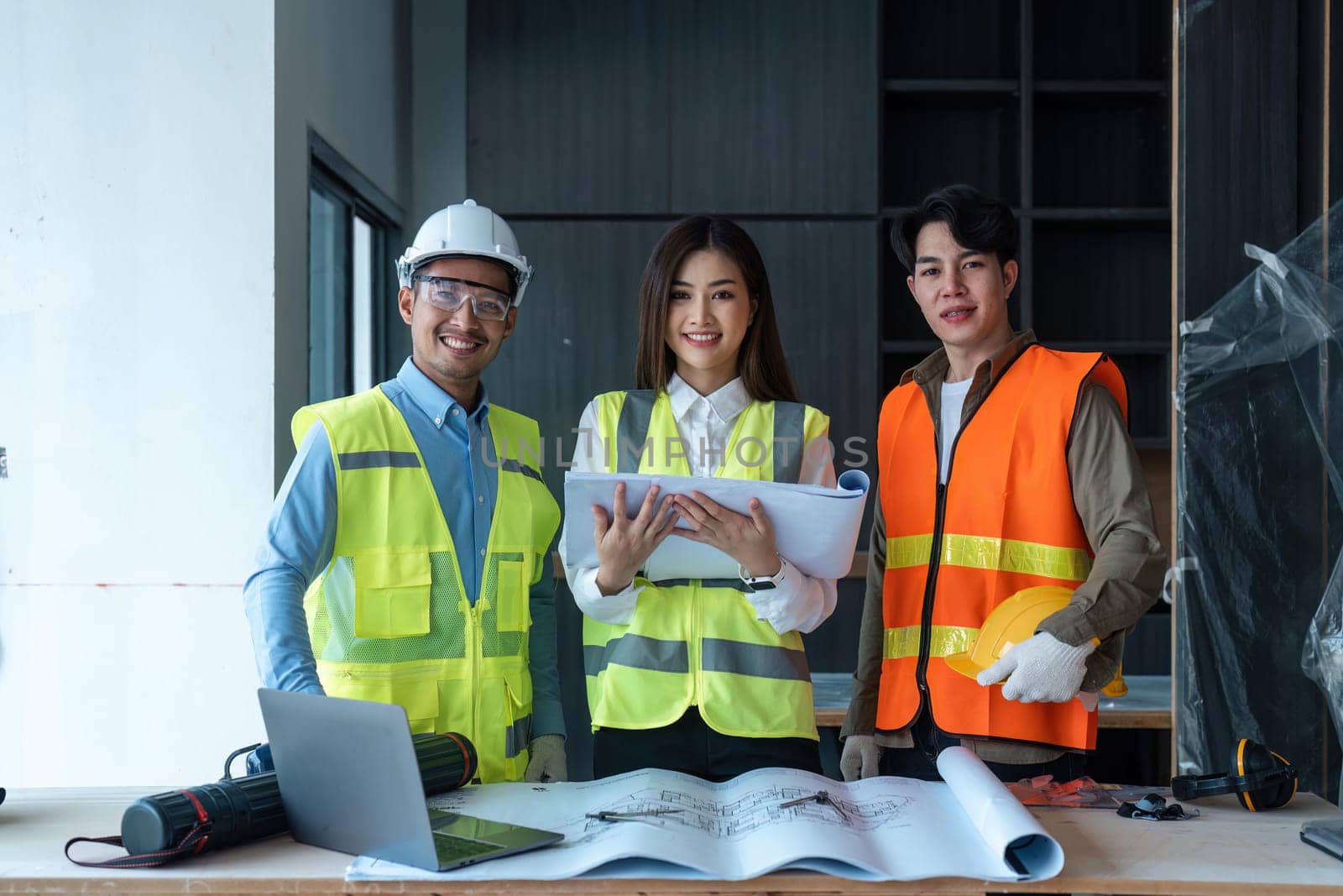 Team of happy confiden engineers wearing safety hard hat and vest standing at site work looking at camera.
