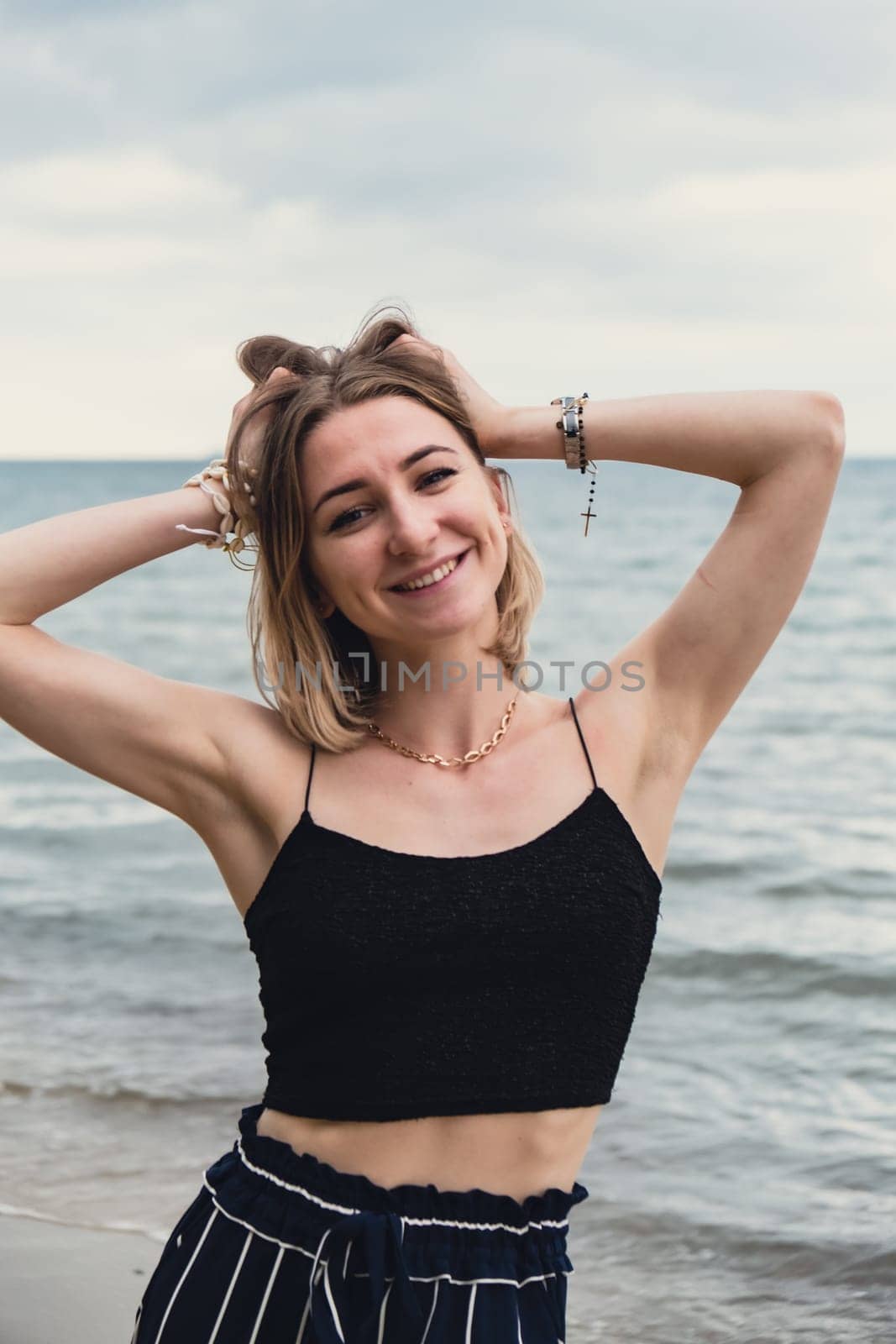 Young woman standing on blurred beachside background. Attractive female enjoying walking the sea shore. travel and active lifestyle concept. Springtime. Relaxation, youth, love, lifestyle solitude with nature. Wellness wellbeing mental health inner peace Slow life digital detox