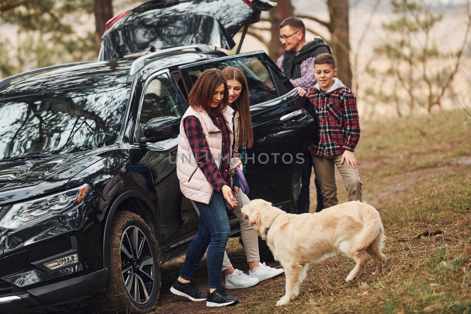 Happy family have fun with their dog near modern car outdoors in forest.