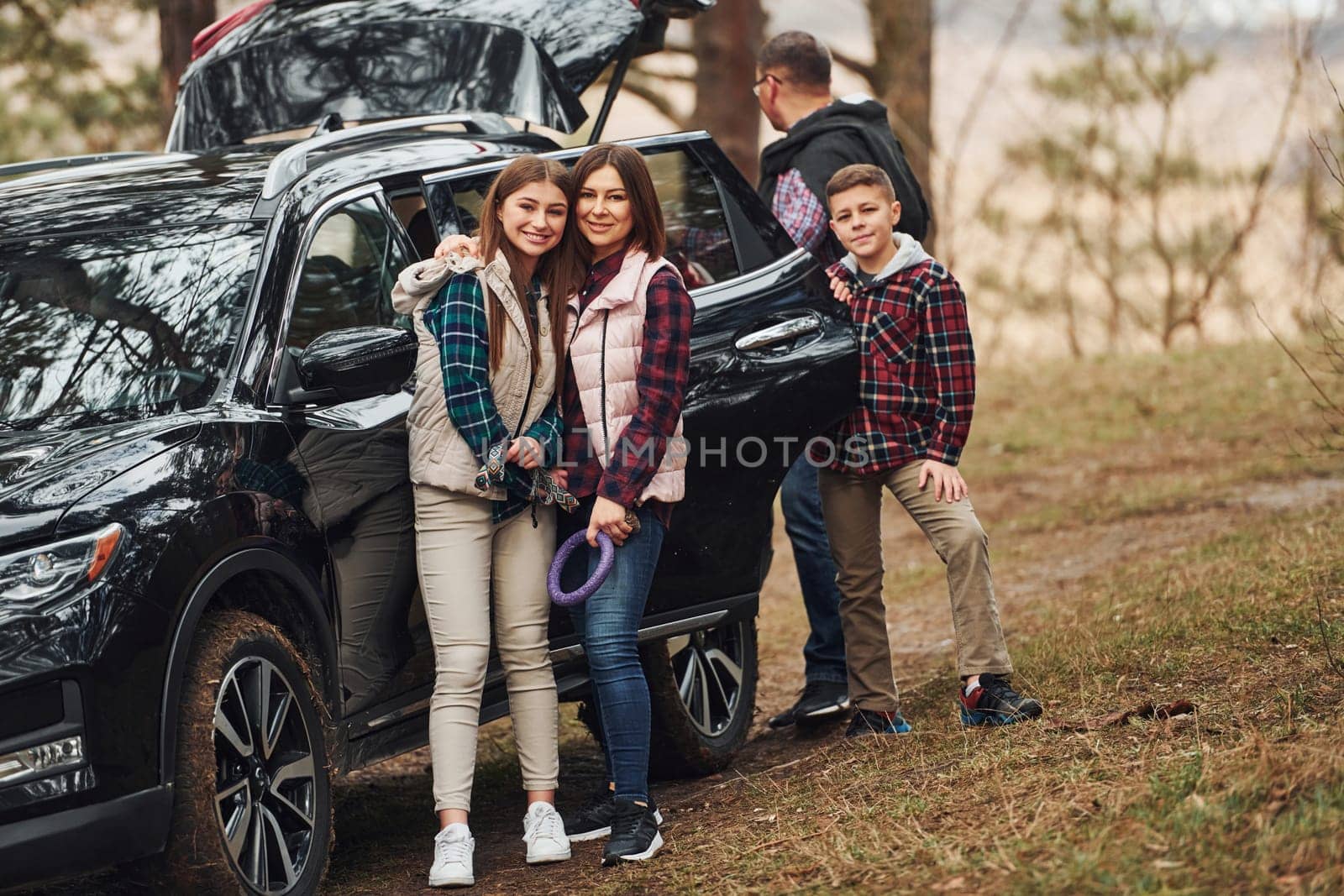 Happy family have fun with their dog near modern car outdoors in forest.