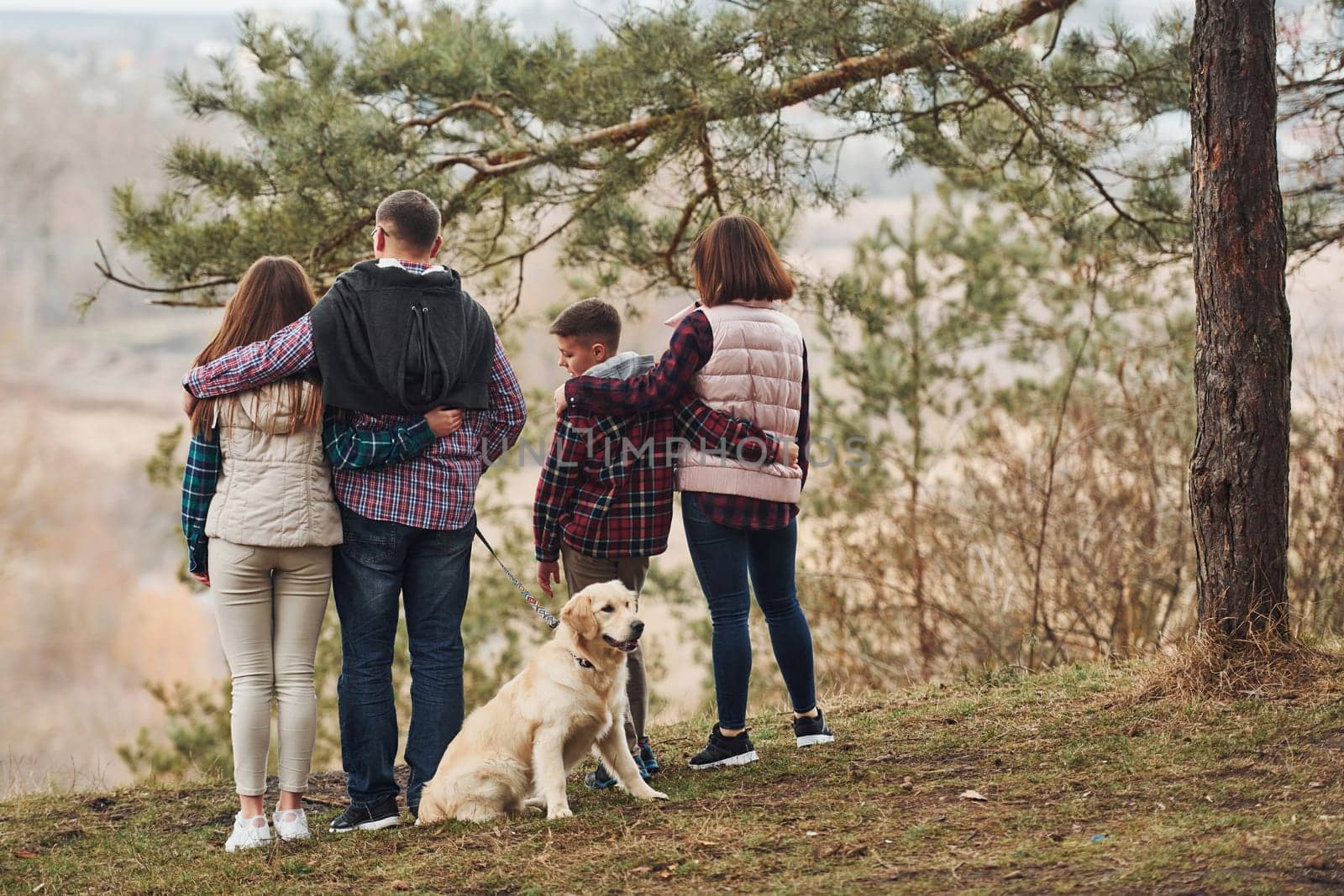 Rear view of family that standing together with their dog outdoors in forest by Standret