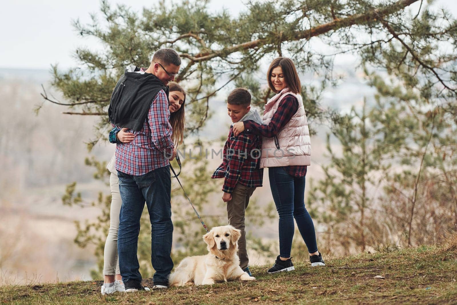 Rear view of family that standing together with their dog outdoors in forest by Standret