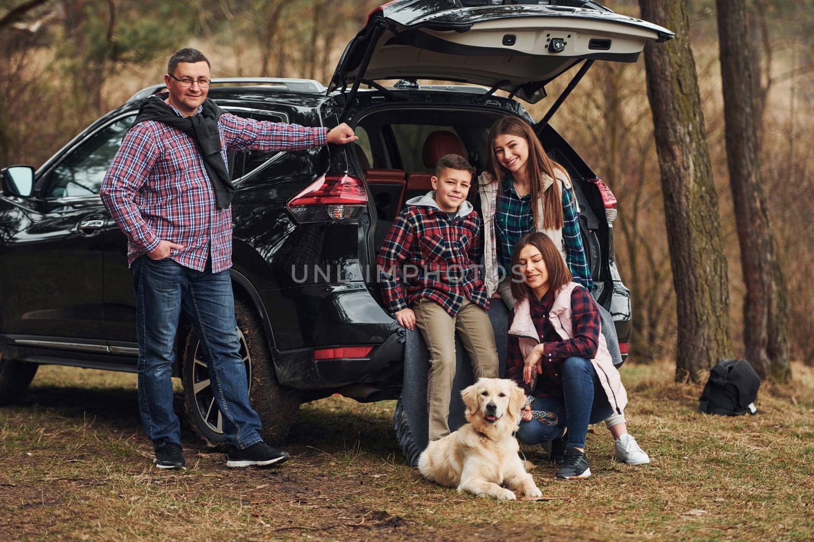 Happy family have fun with their dog near modern car outdoors in forest.