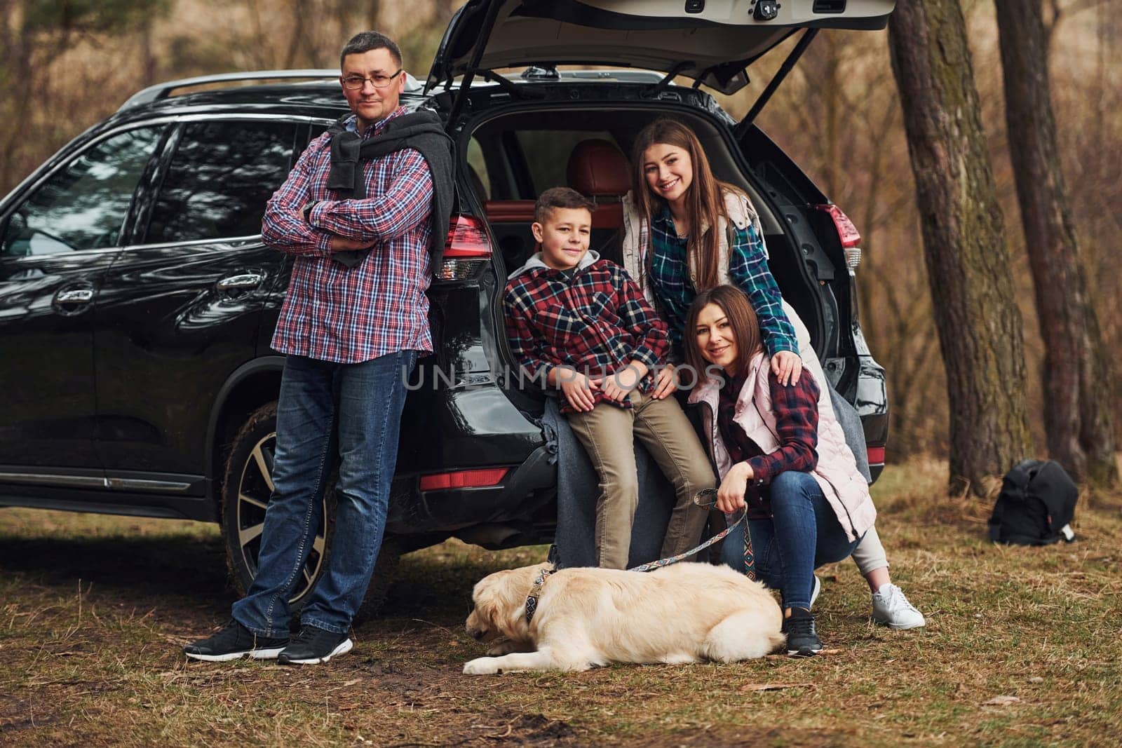 Happy family have fun with their dog near modern car outdoors in forest by Standret