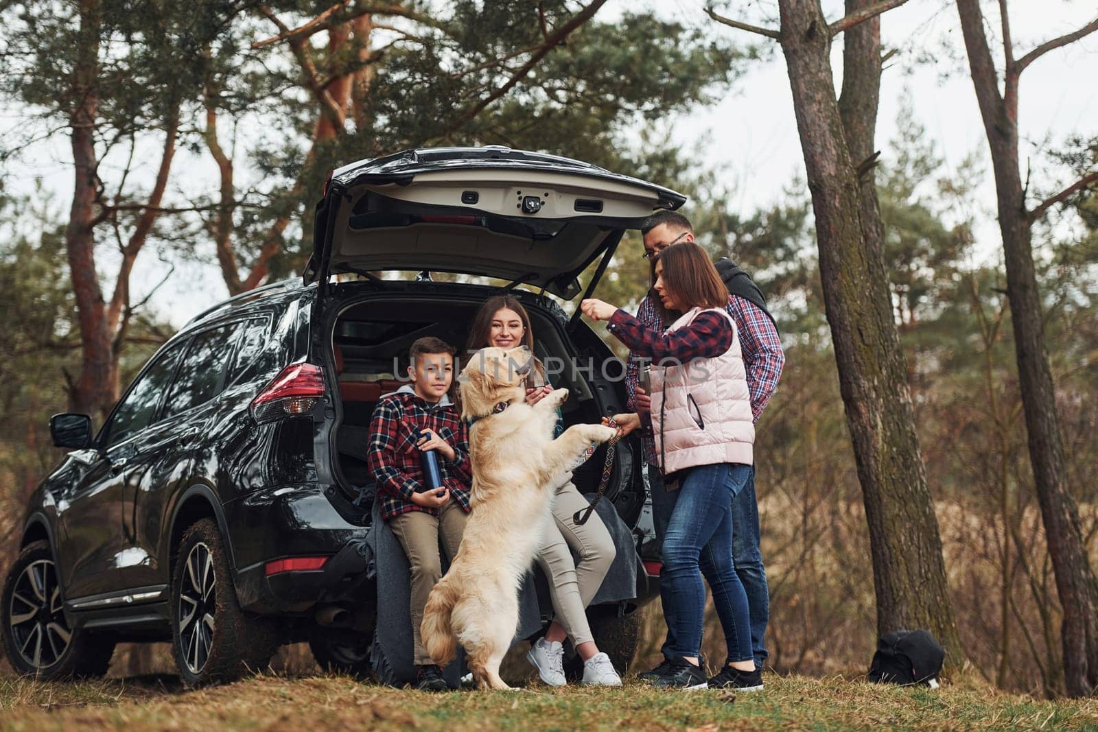 Happy family have fun with their dog near modern car outdoors in forest.