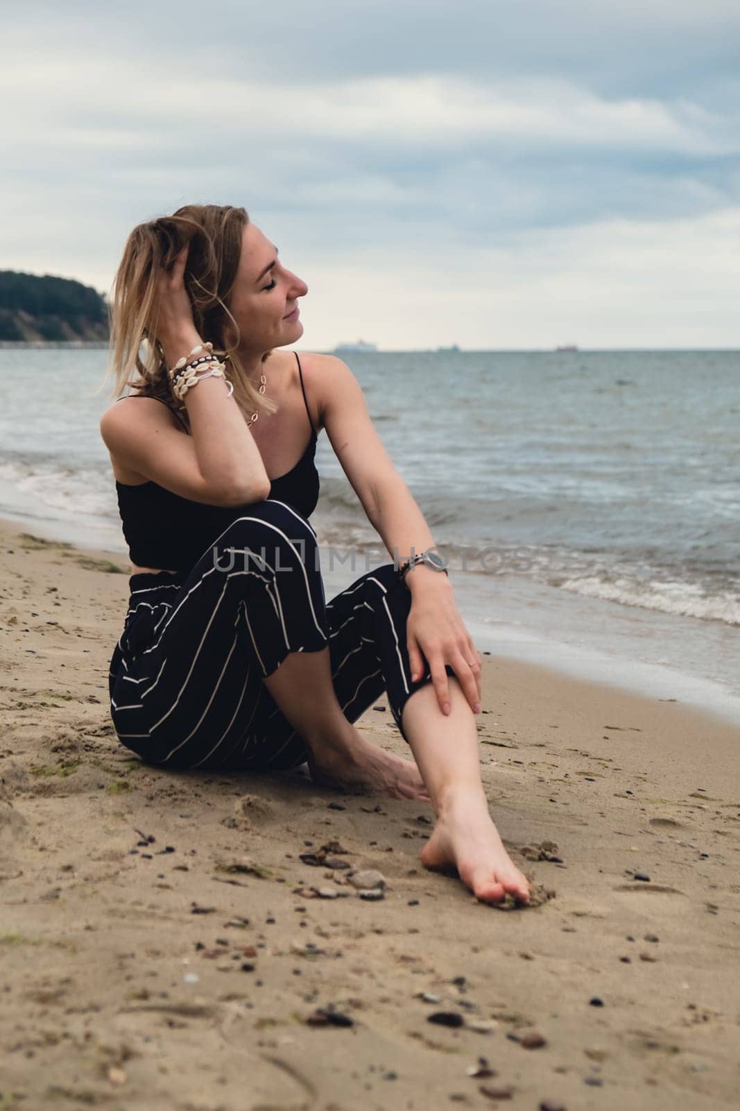 Young woman siting on blurred beachside background. Attractive female enjoying the sea shore. travel and active lifestyle concept. Springtime. Relaxation, youth, love, lifestyle solitude with nature. Wellness wellbeing mental health inner peace Slow life digital detox