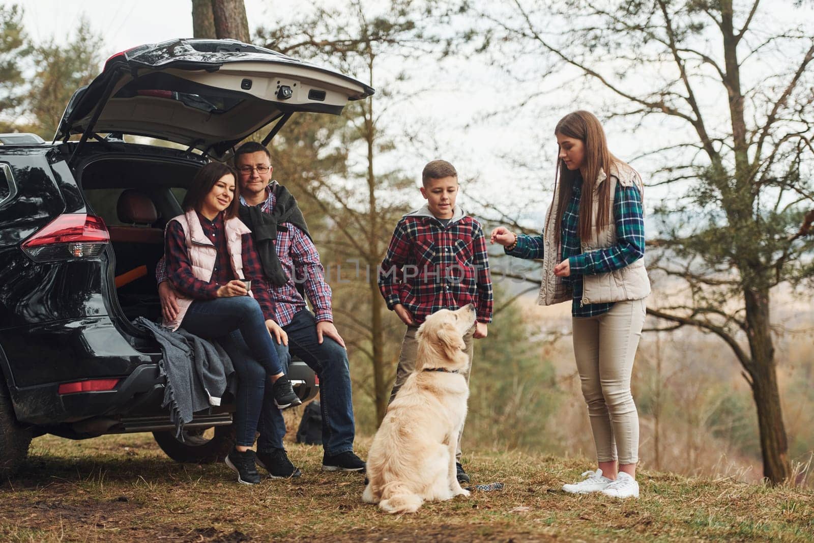 Happy family have fun with their dog near modern car outdoors in forest by Standret