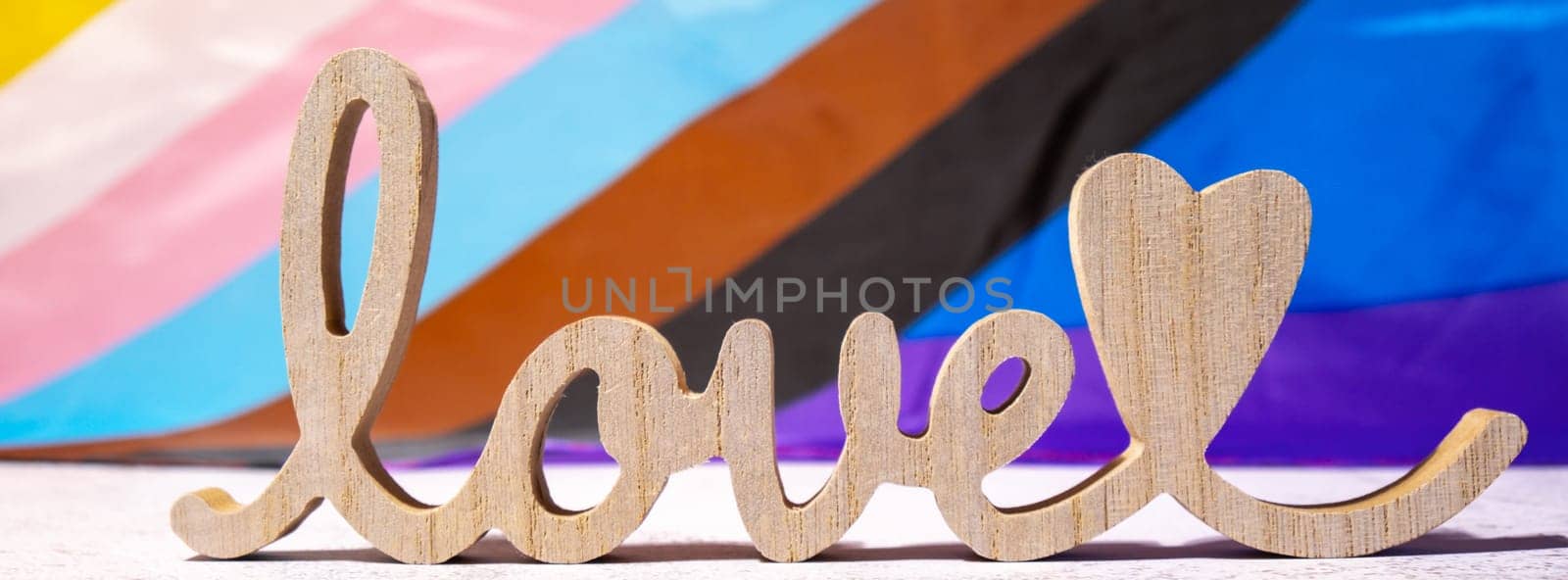 Banner Wooden word love with heart romance on Rainbow LGBTQIA flag made from silk material. Valentine's Day greeting card. Symbol of LGBTQ pride month. Equal rights. Peace and freedom. Support LGBTQIA community by anna_stasiia