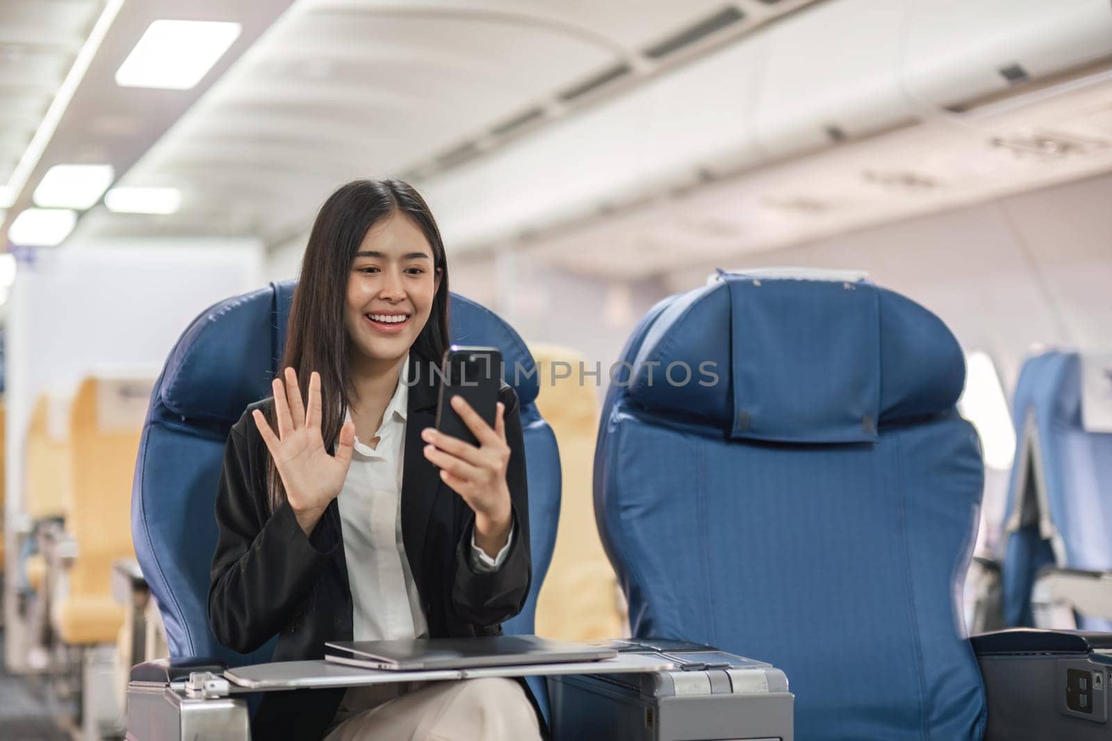 Young woman sitting with phone video call on the aircraft seat near the window during the flight in the airplane by nateemee