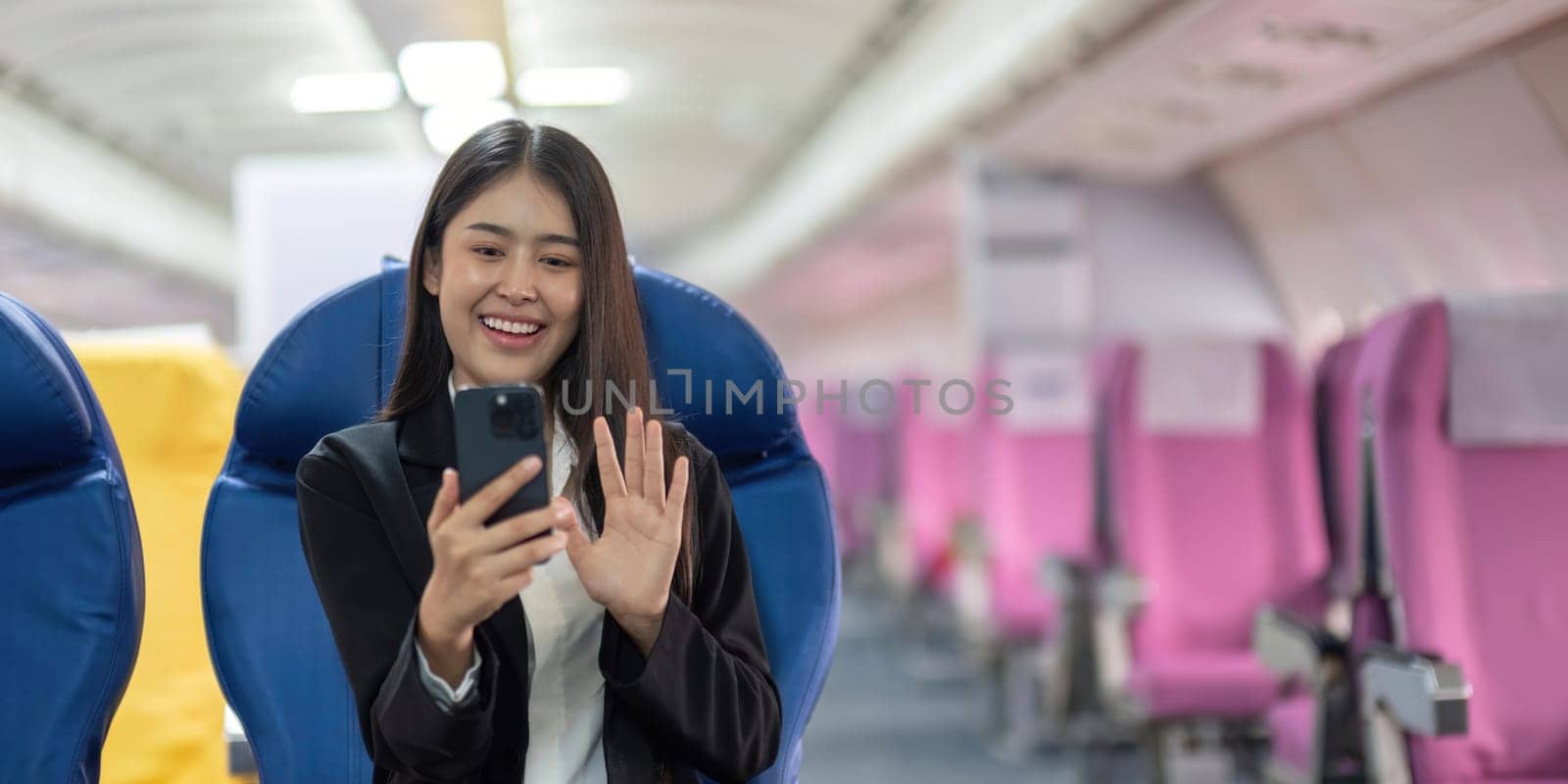 Young woman sitting with phone video call on the aircraft seat near the window during the flight in the airplane.