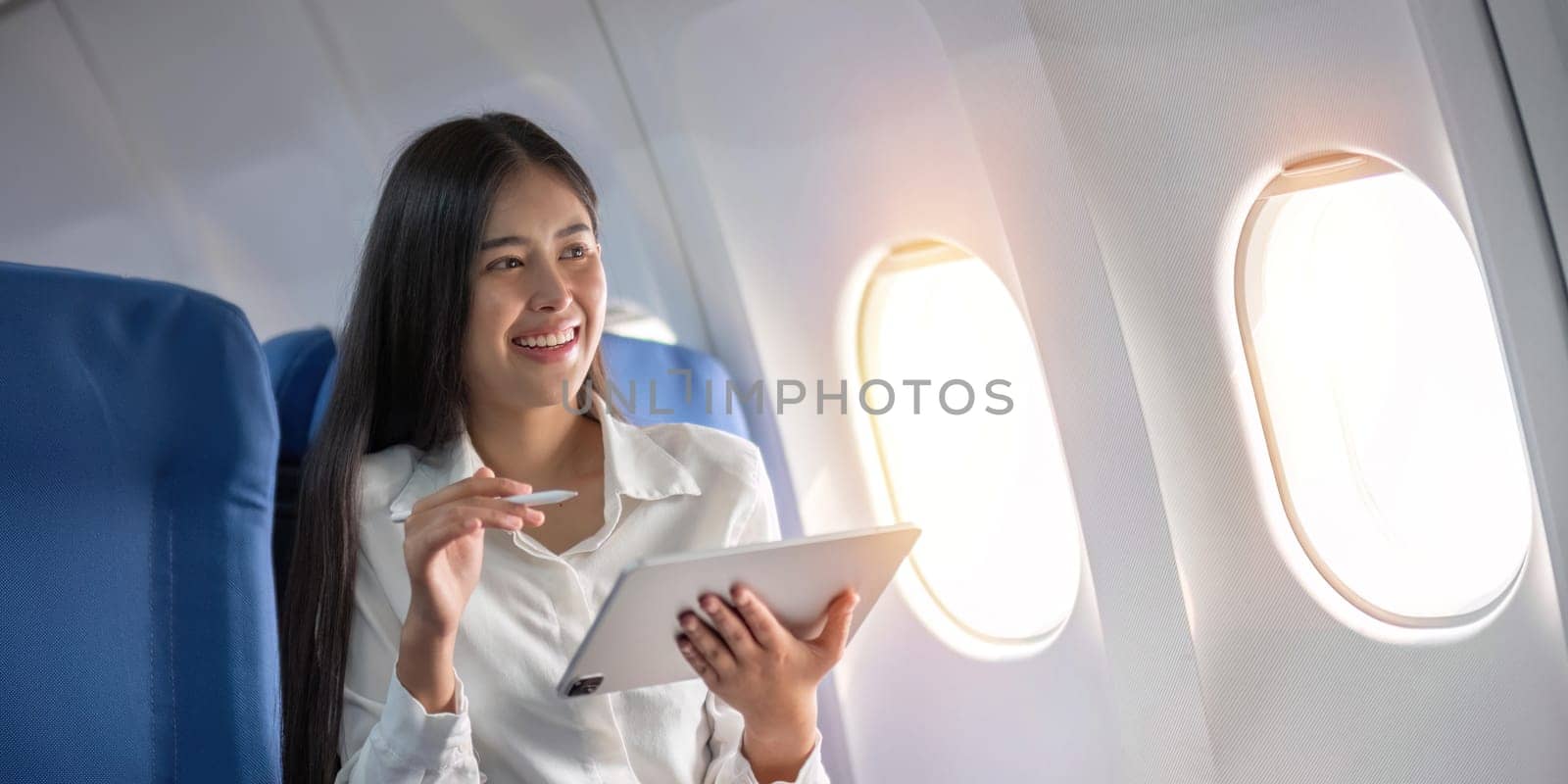 Beautiful asian travel woman watching movie on digital tablet in airplane by nateemee