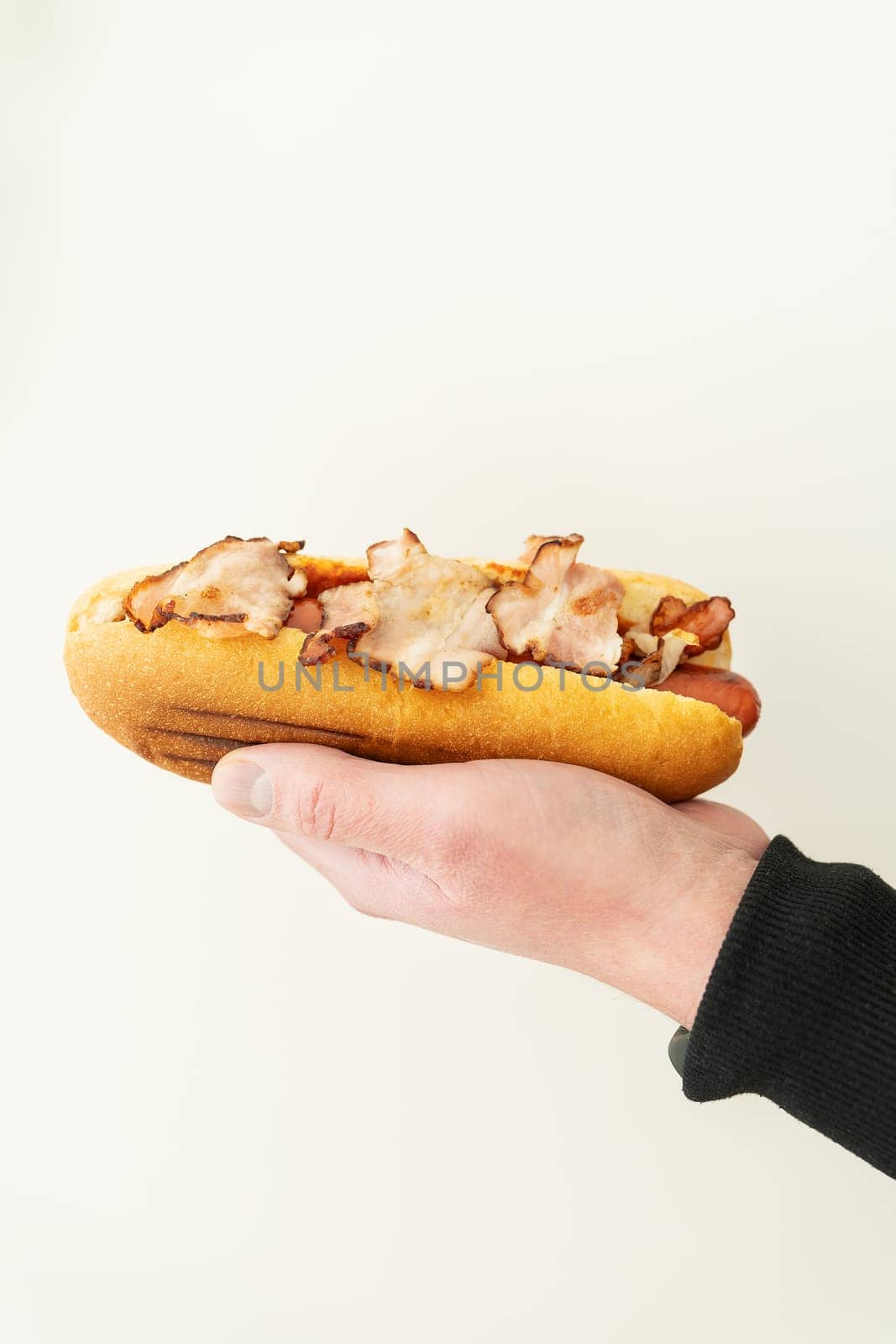 Cropped view of young guy holding tasty hot dog with mustard and ketchup on white background. Street food, delivery