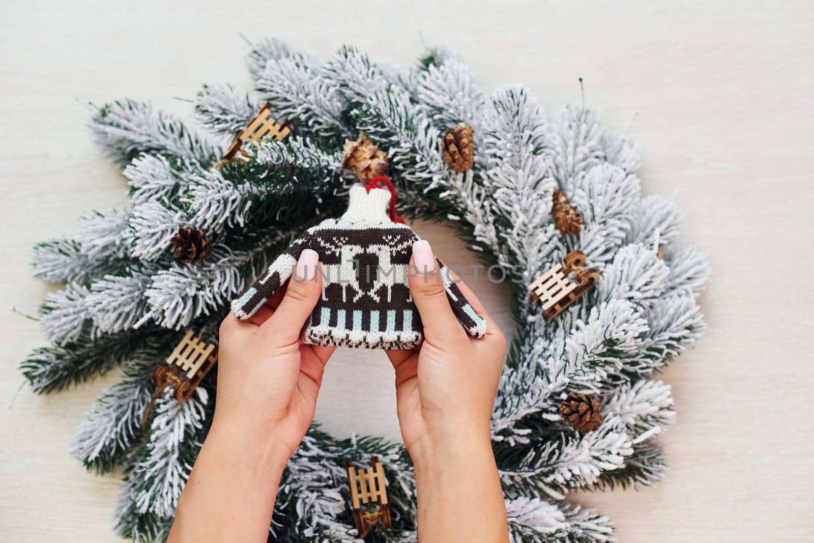 Woman's hands holds little sweater. Top view of christmas festive texture with new year decorations.