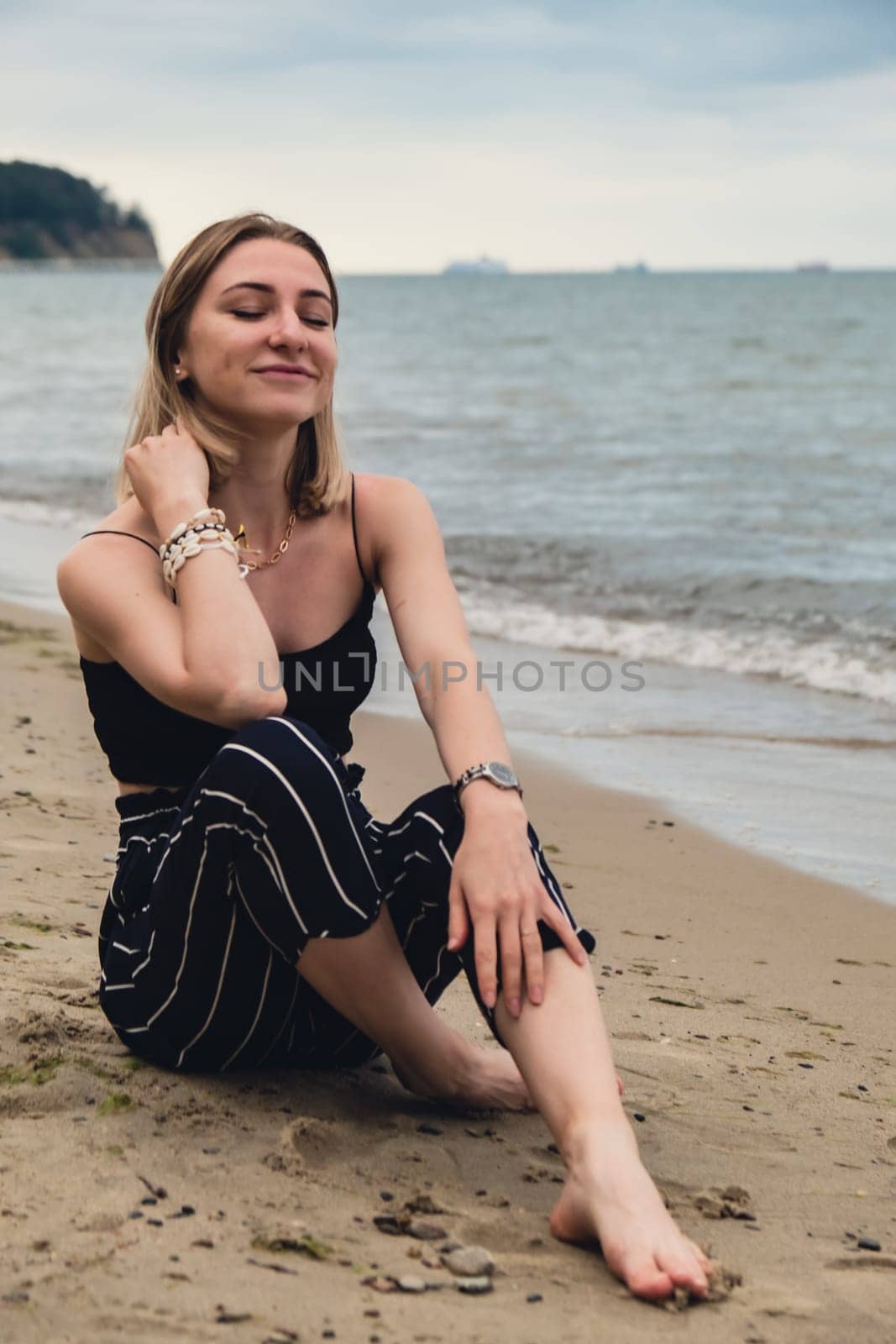 Young woman siting on blurred beachside background. Attractive female enjoying the sea shore. travel and active lifestyle concept. Springtime. Relaxation, youth, love, lifestyle solitude with nature. Wellness wellbeing mental health inner peace Slow life digital detox