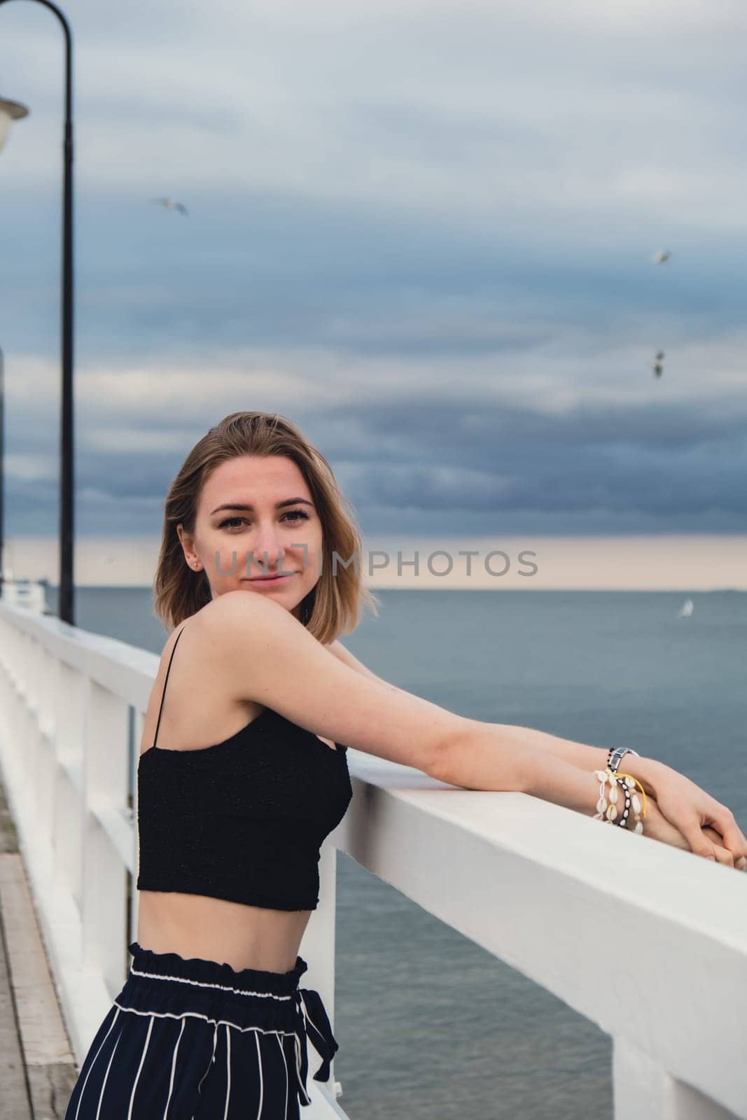 Young woman standing on wooden pier blurred beachside background. Attractive female enjoying the sea shore travel and active lifestyle concept. Springtime. Wellness wellbeing mental health inner peace Slow life digital detox