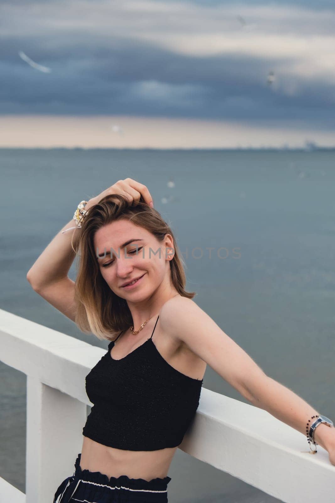 Young woman standing on wooden pier blurred beachside background. Attractive female enjoying the sea shore travel and active lifestyle concept. Springtime. Wellness wellbeing mental health inner peace Slow life digital detox