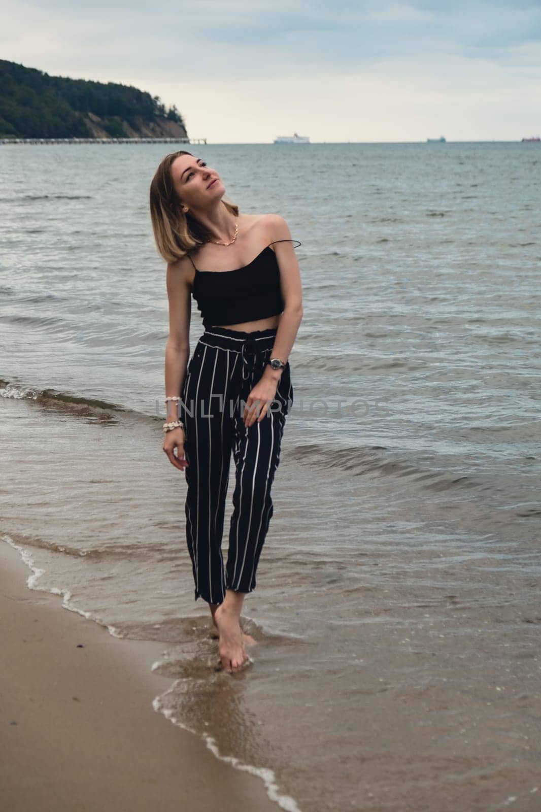 Young woman standing on blurred beachside background. Attractive female enjoying walking the sea shore. travel and active lifestyle concept. Springtime. Relaxation, youth, love, lifestyle solitude with nature. Wellness wellbeing mental health inner peace Slow life digital detox