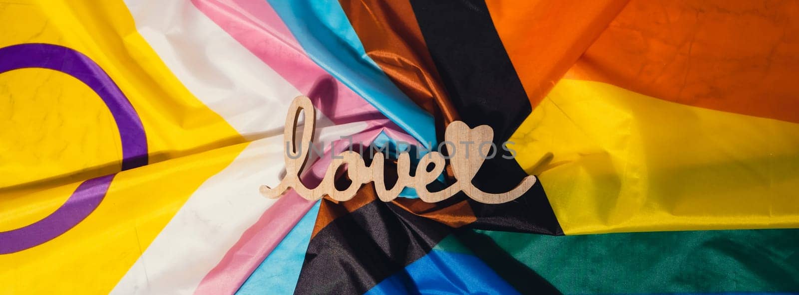 Banner Wooden word love with heart romance on Rainbow LGBTQIA flag made from silk material. Valentine's Day greeting card. Symbol of LGBTQ pride month. Equal rights. Peace and freedom. Support LGBTQIA community. Diversity equality