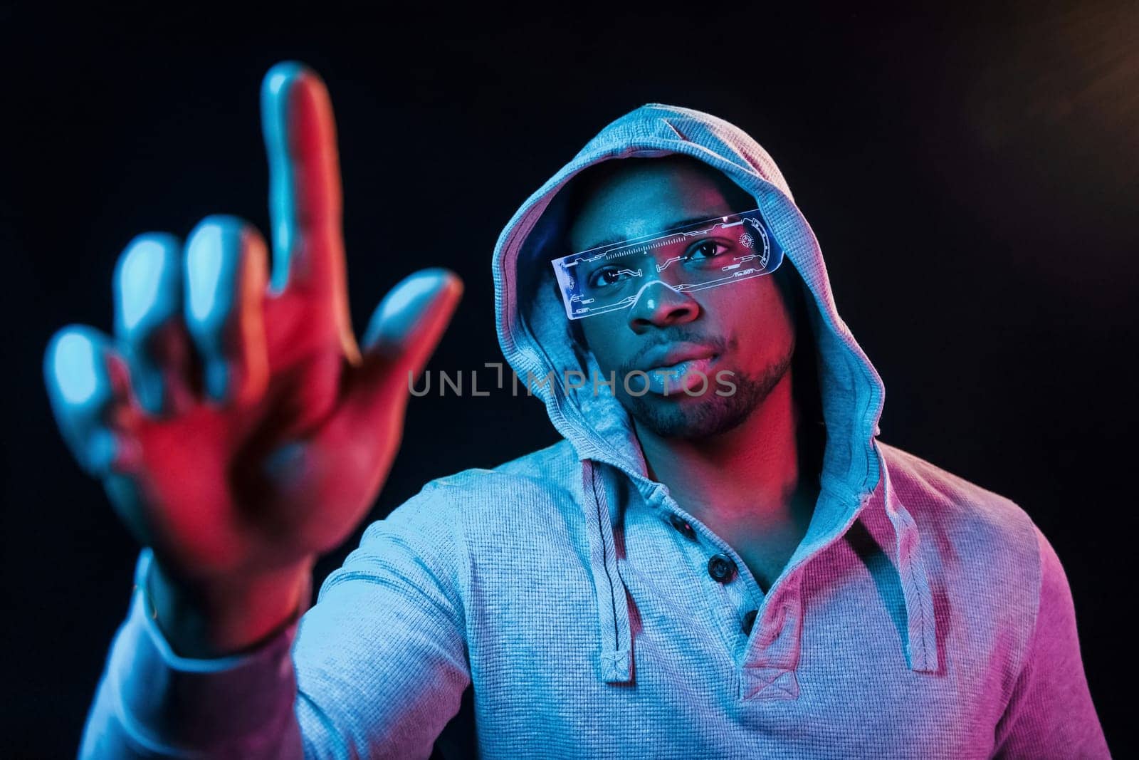 In special eyewear. Futuristic neon lighting. Young african american man in the studio by Standret