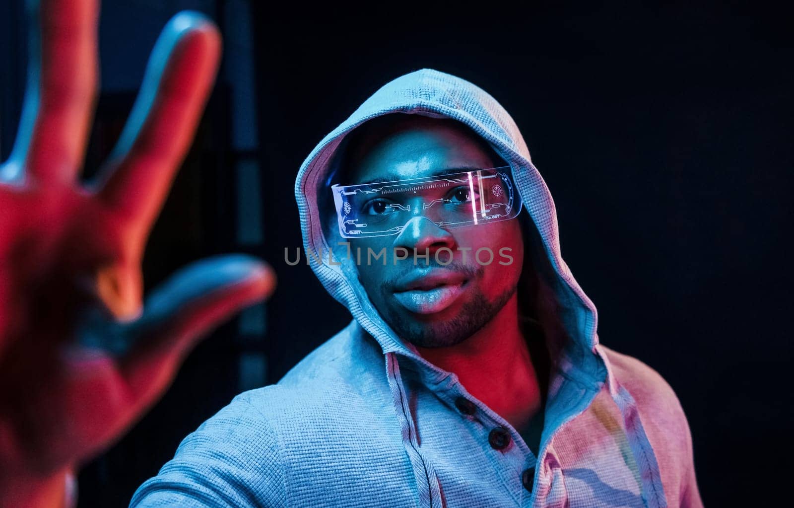 In special eyewear. Futuristic neon lighting. Young african american man in the studio.