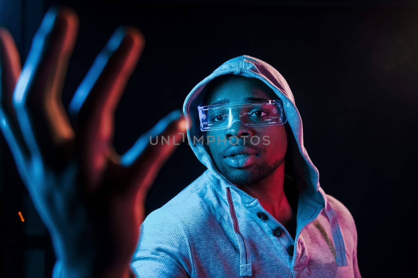 In special eyewear. Futuristic neon lighting. Young african american man in the studio.