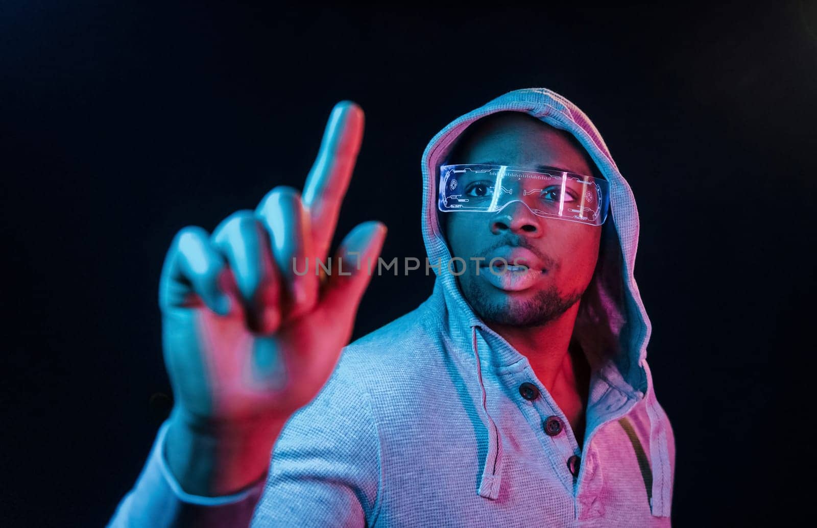 In special eyewear. Futuristic neon lighting. Young african american man in the studio.