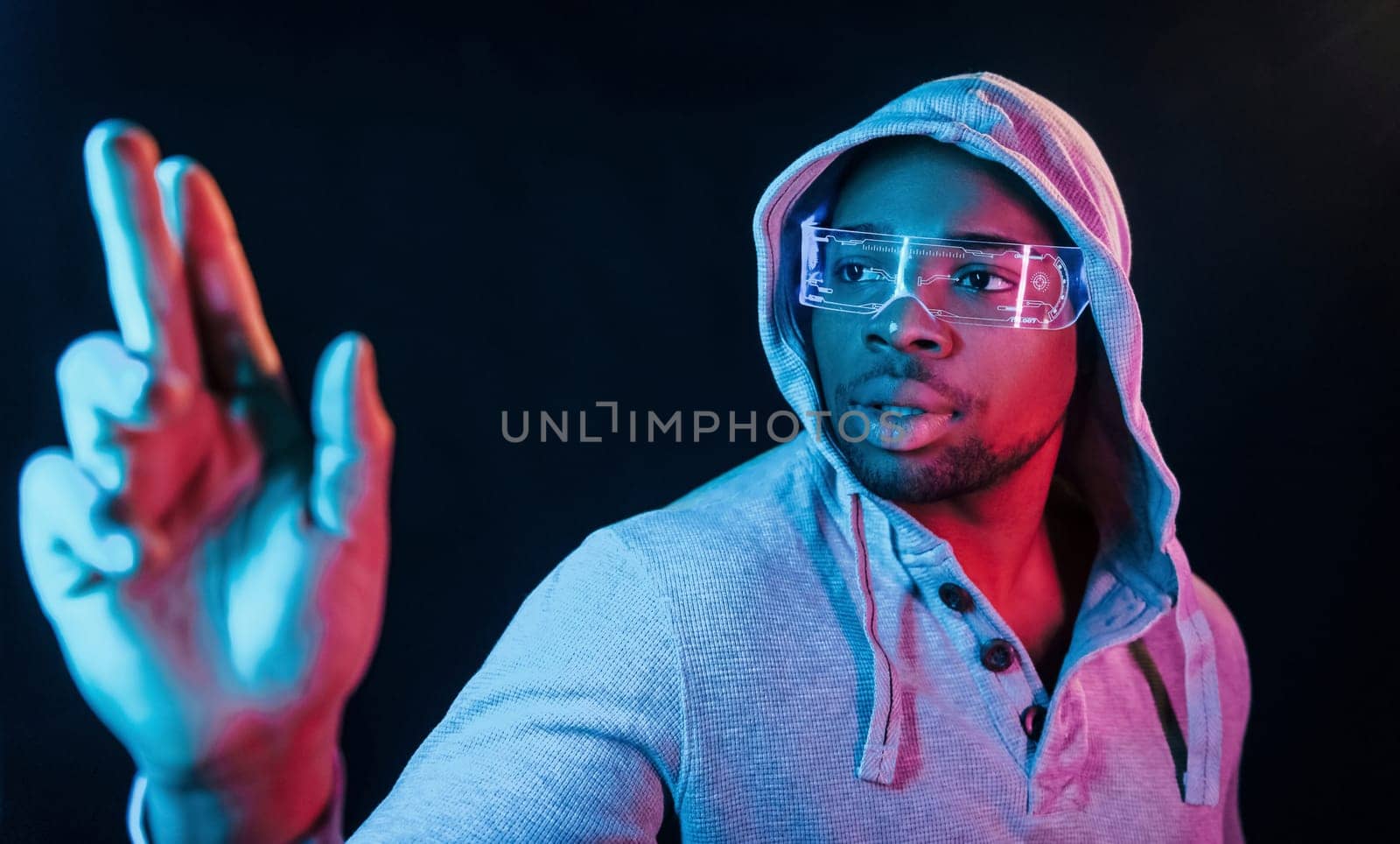 In special eyewear. Futuristic neon lighting. Young african american man in the studio.