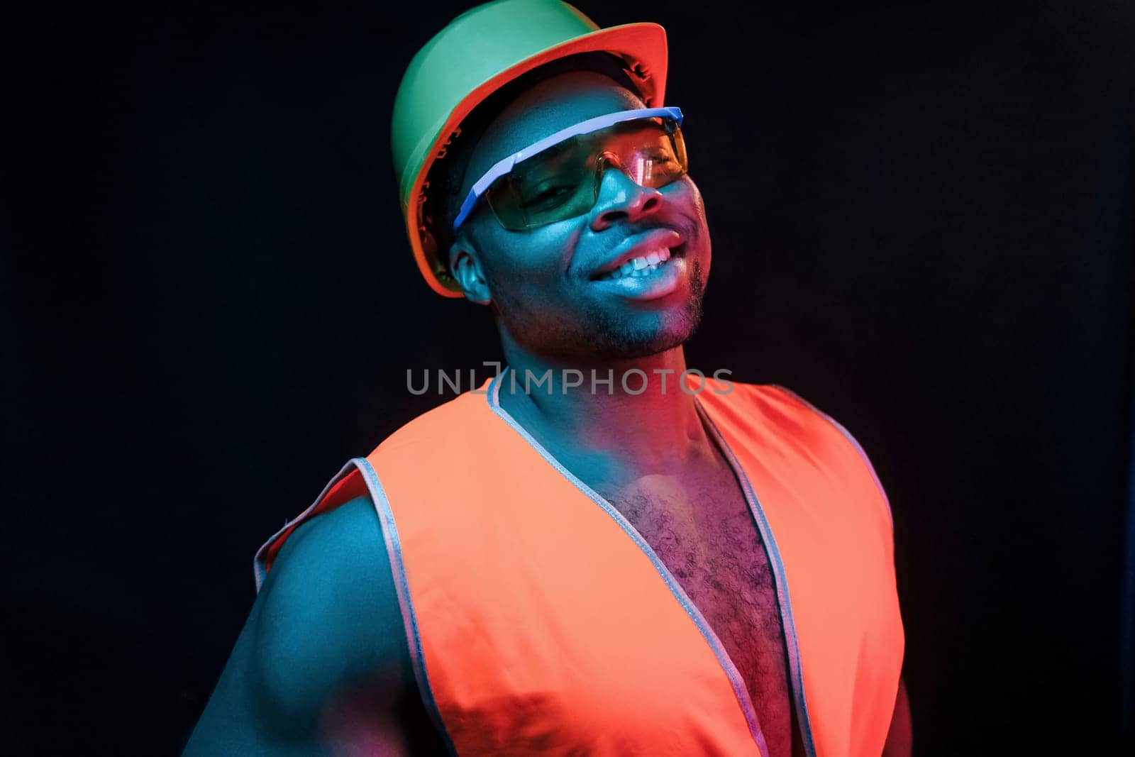 Construction worker in uniform and hard hat. Futuristic neon lighting. Young african american man in the studio.