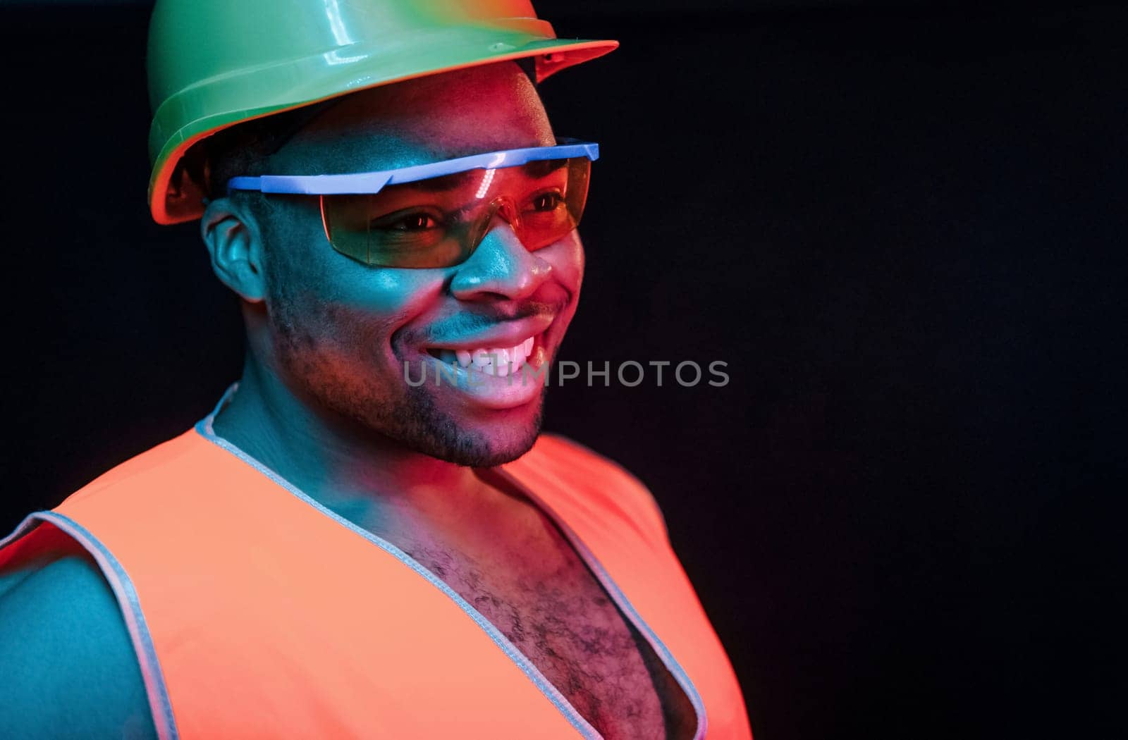 Construction worker in uniform and hard hat. Futuristic neon lighting. Young african american man in the studio.