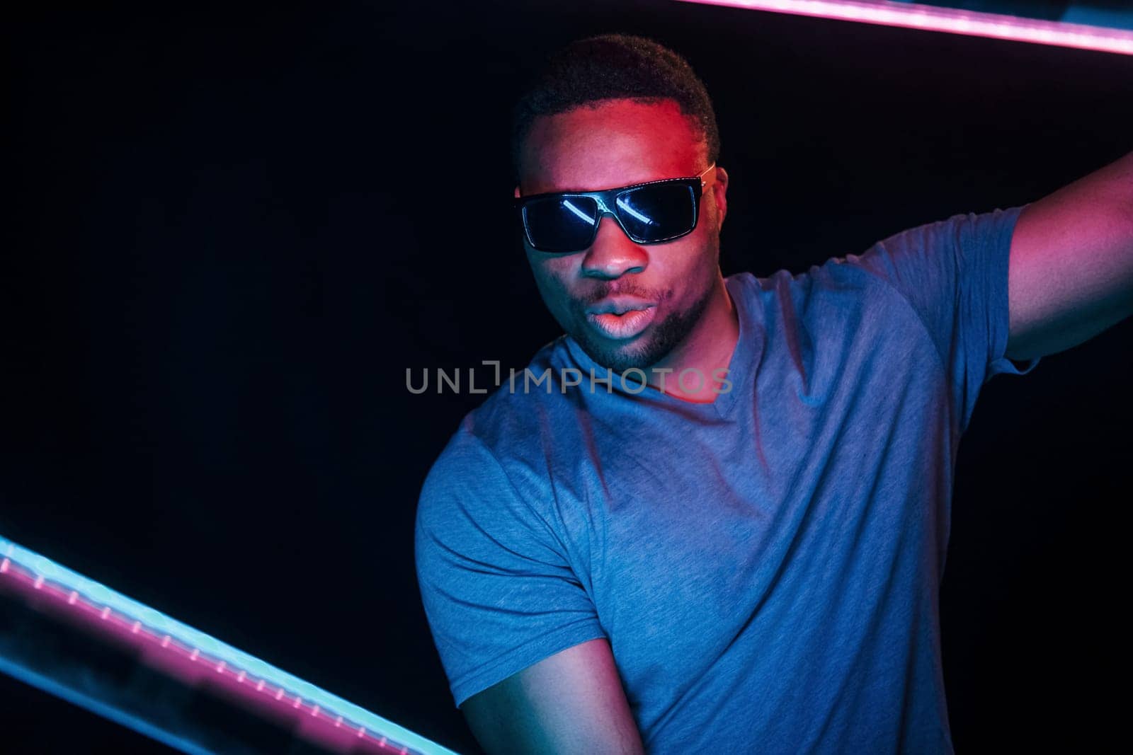 With sunglasses. Futuristic neon lighting. Young african american man in the studio.