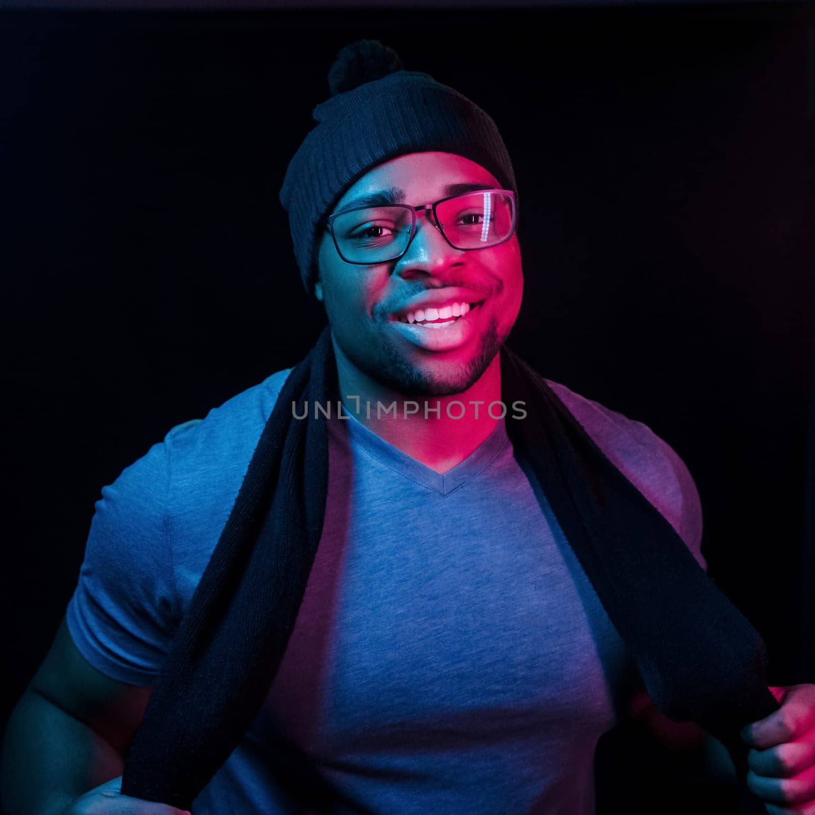 In hat and scarf. Futuristic neon lighting. Young african american man in the studio by Standret