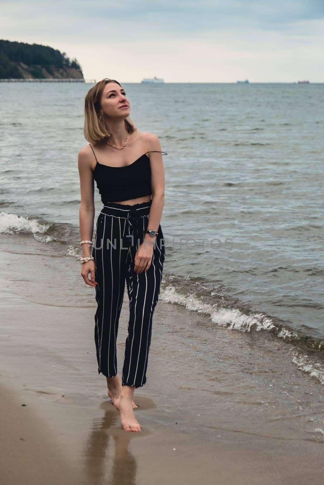 Young woman standing on blurred beachside background. Attractive female enjoying walking the sea shore. travel and active lifestyle concept. Springtime. Relaxation, youth, love, lifestyle solitude with nature. Wellness wellbeing mental health inner peace Slow life digital detox