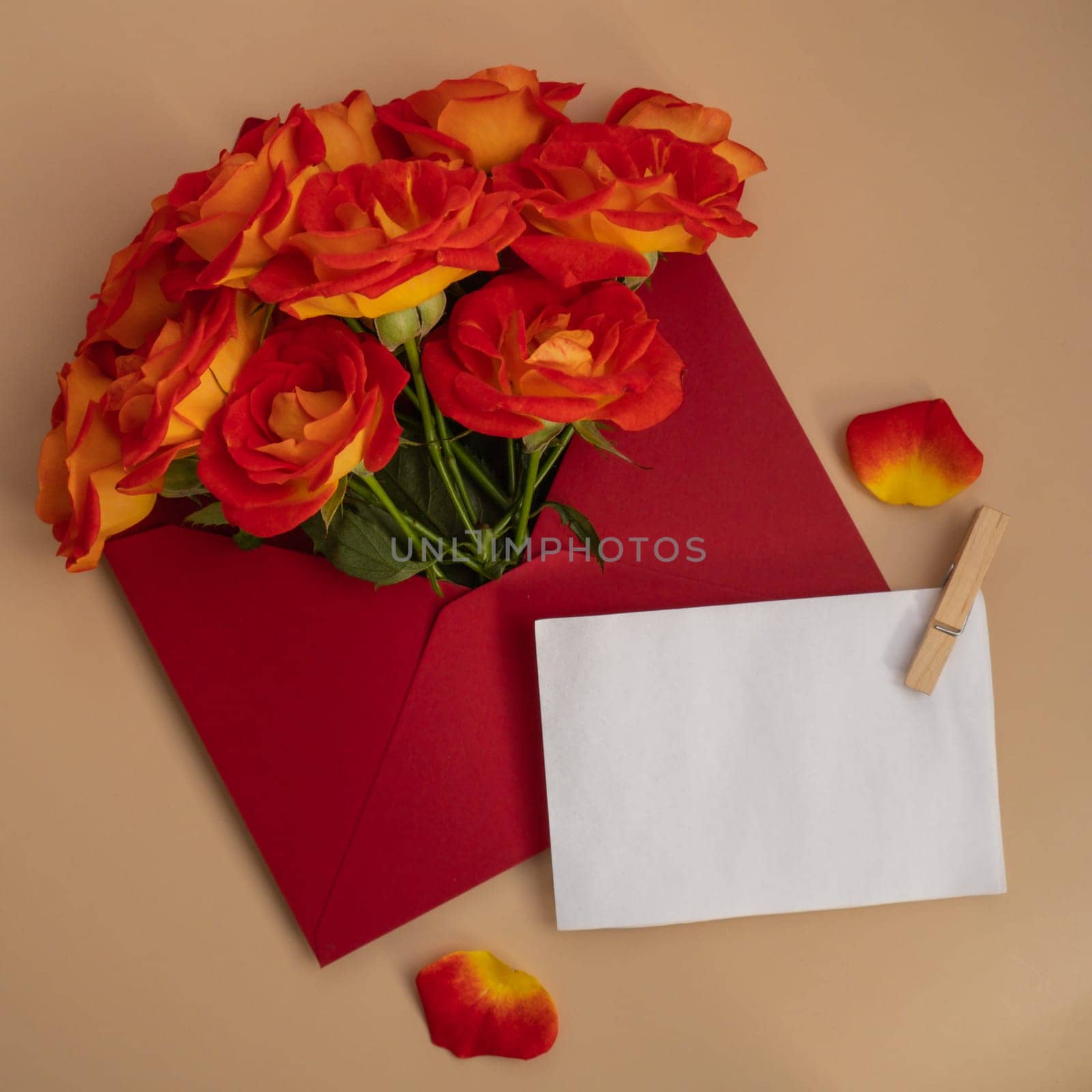 Beautiful red roses flowers in postal red envelope on neutral beige background, empty paper note copy space for text, spring time, greeting card for holiday. Flower delivery. Delicate red yellow roses. Minimal trendy composition. Romantic pastel flowers by anna_stasiia