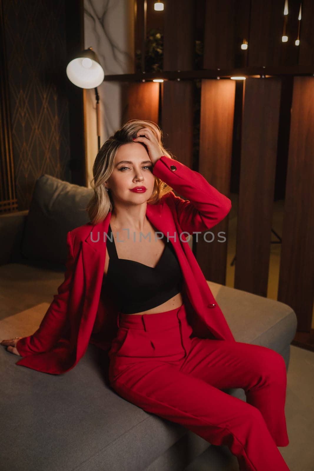 a beautiful girl dressed in a red formal suit posing in a modern interior.