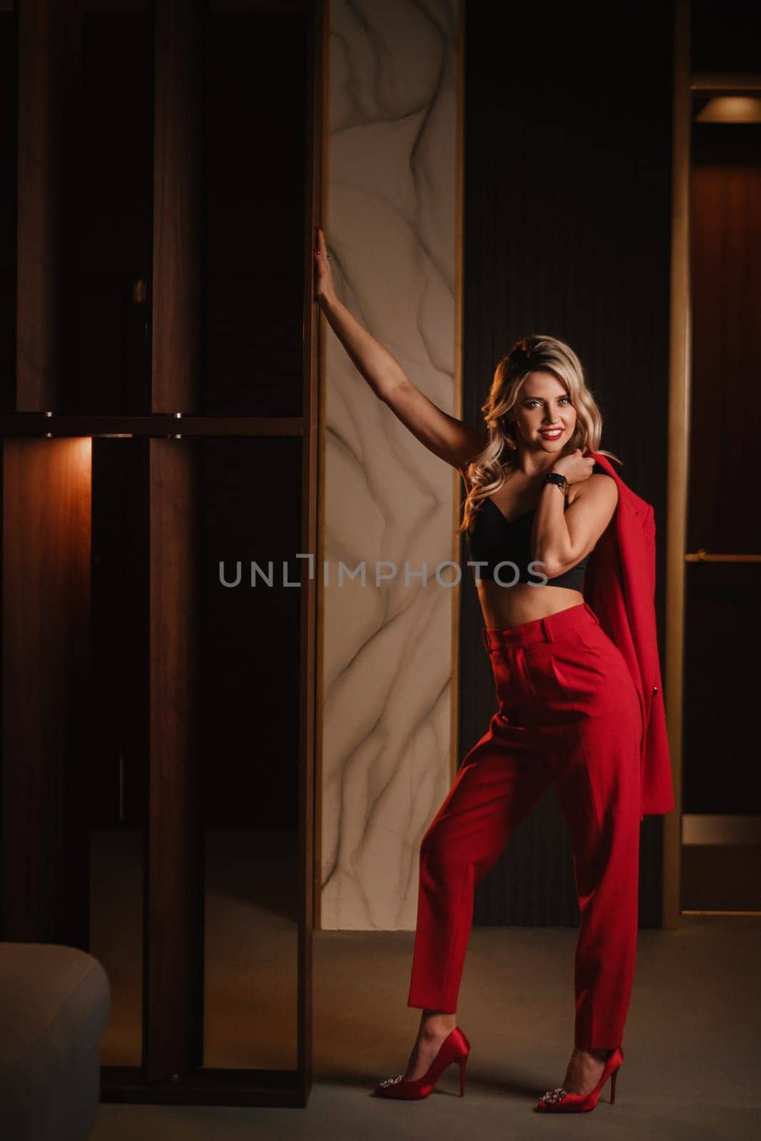 a beautiful girl dressed in a red formal suit posing in a modern interior.